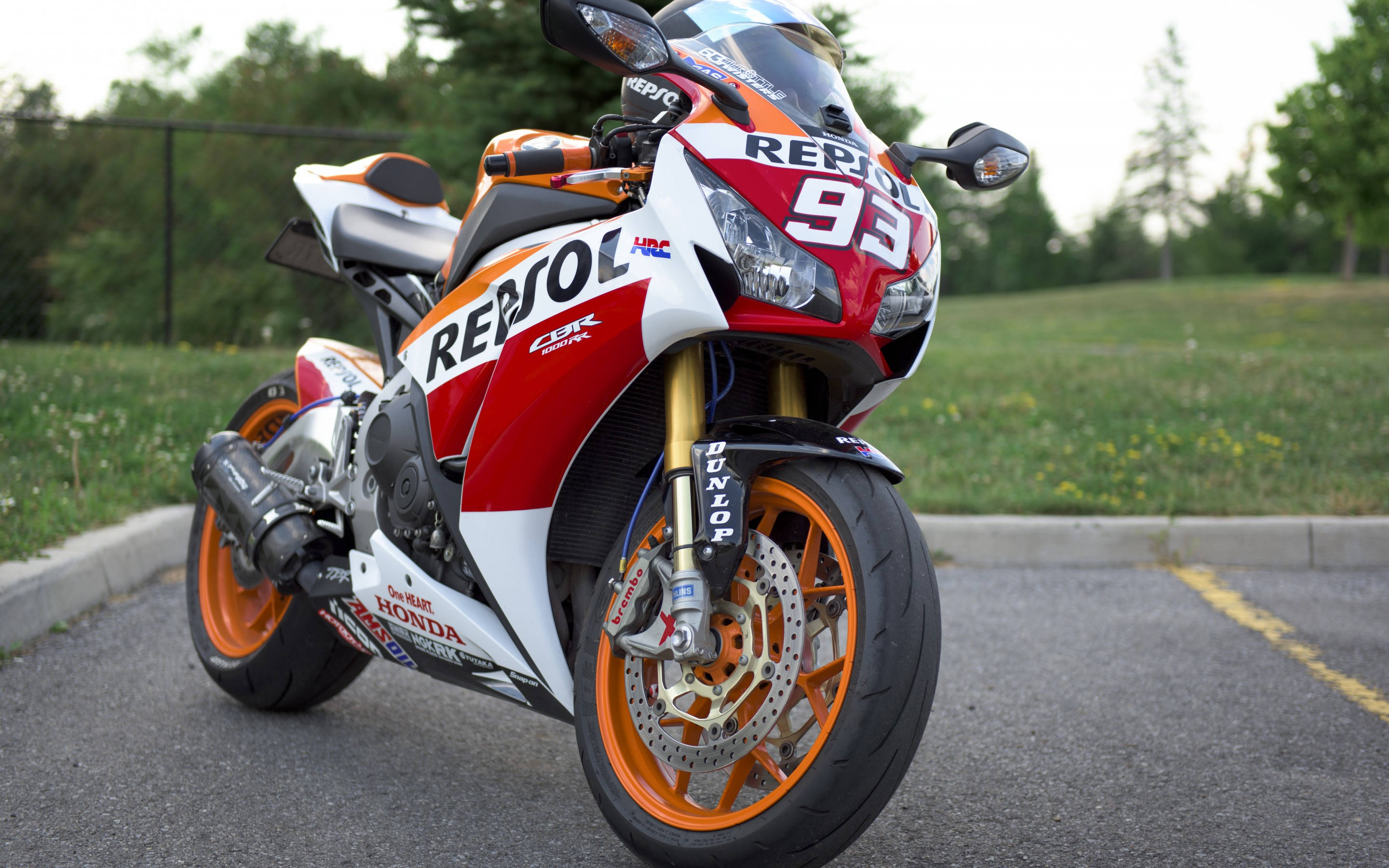 Honda 桌布 壁紙 — 一輛紅色、白色和橙色的 Repsol Honda CBR 摩托車，號碼 93，停放在瀝青路上，靠近草地。