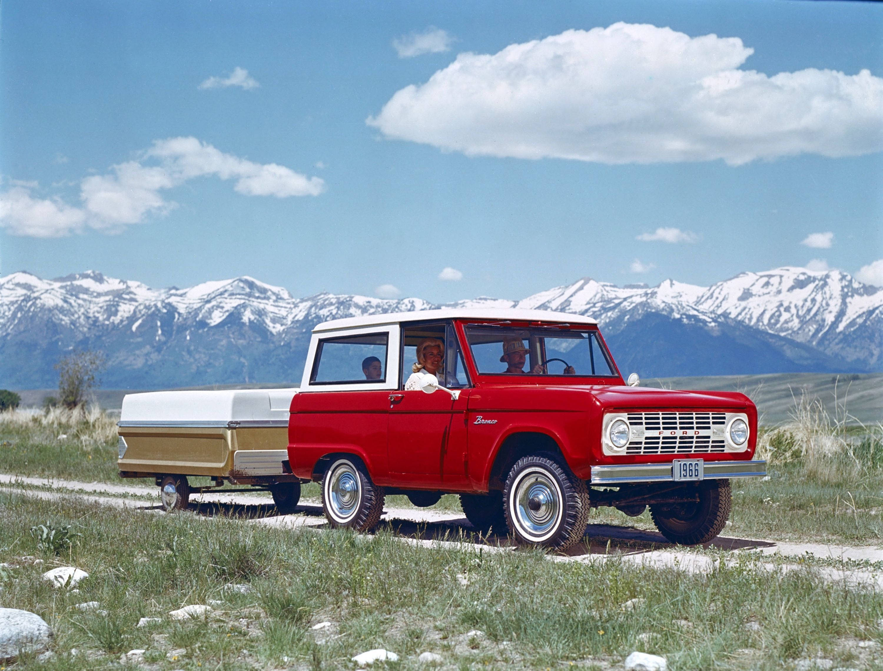 old 桌布 壁紙 — 一輛紅色1966年福特Bronco，白色車頂，在藍天白雲下，背景是積雪的山峰，行駛在長滿草的泥土路上。