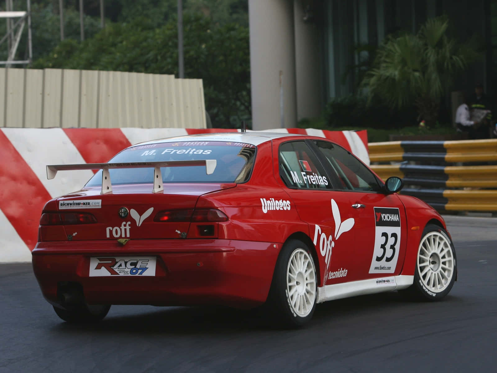 Alfa Romeo 156 桌布 壁紙 — 一輛紅色33號賽車在紅白護欄和綠色植物環繞的賽道上疾馳。