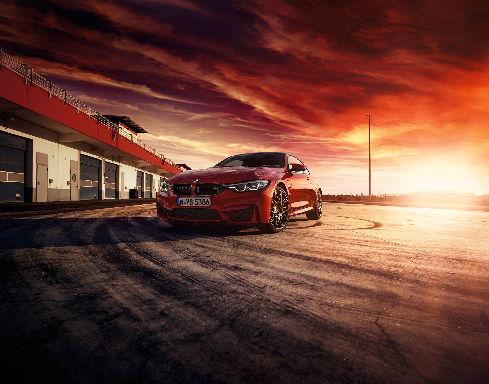 紅色BMW M4跑車在賽道上，夕陽天空戲劇性，輪胎痕清晰可見。