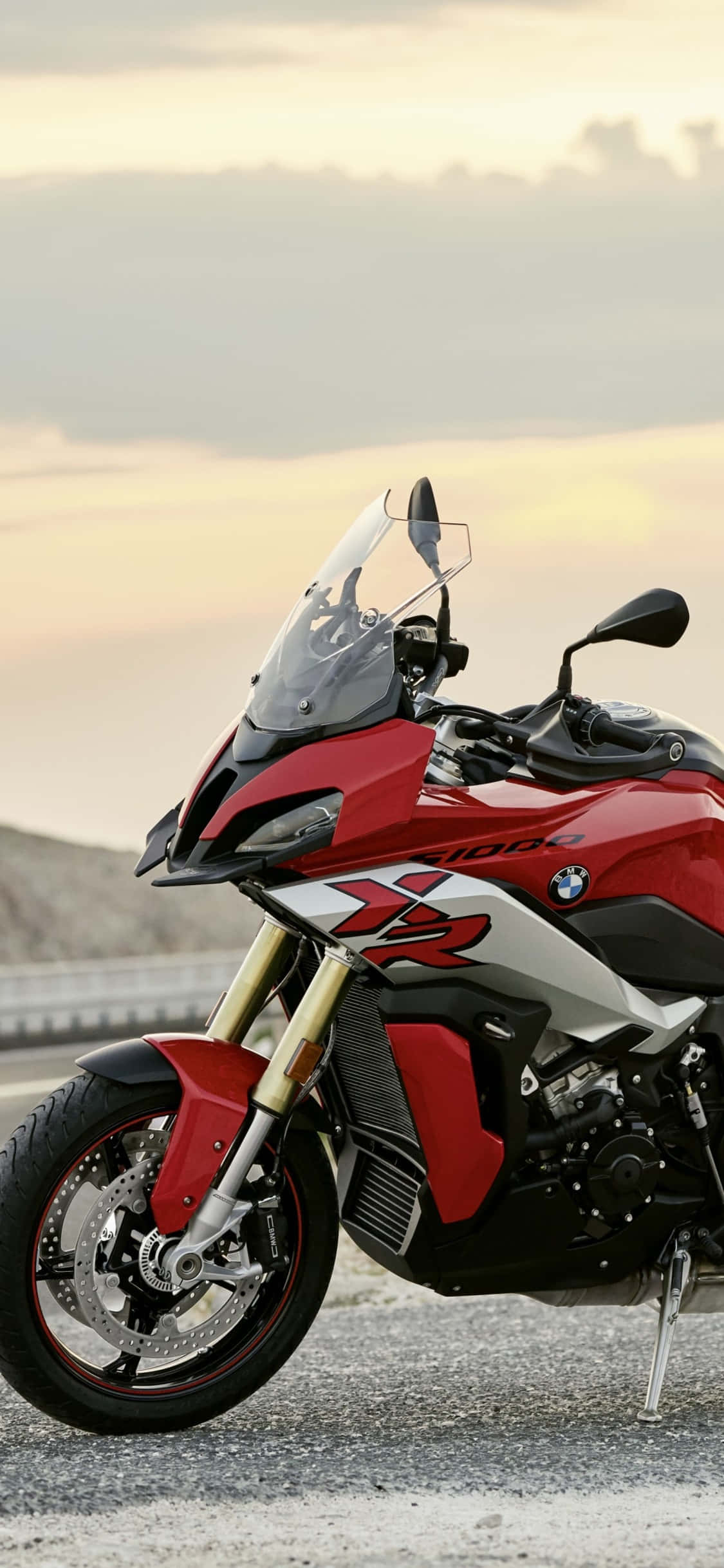 iPhone X Bmw 桌布 壁紙 — 一輛紅色BMW R 1200 GS冒險摩托車停在碎石路邊，背景是柔和的金色日落天空。