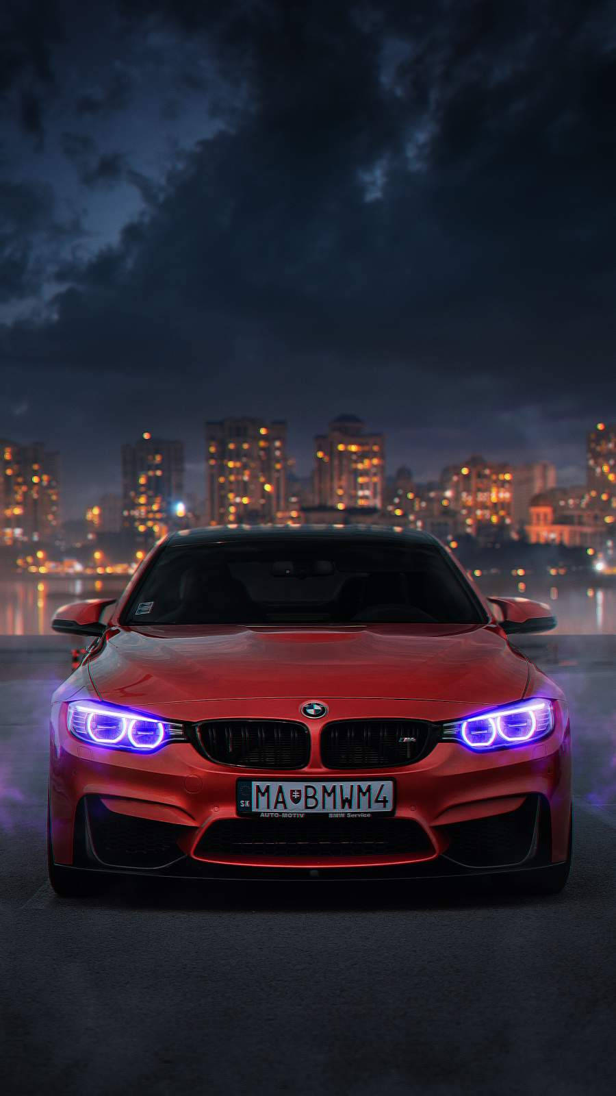 紅色BMW跑車配備藍色車頭燈，夜晚停放在城市中，背景有燈光建築。 — BMW 動圖 壁紙