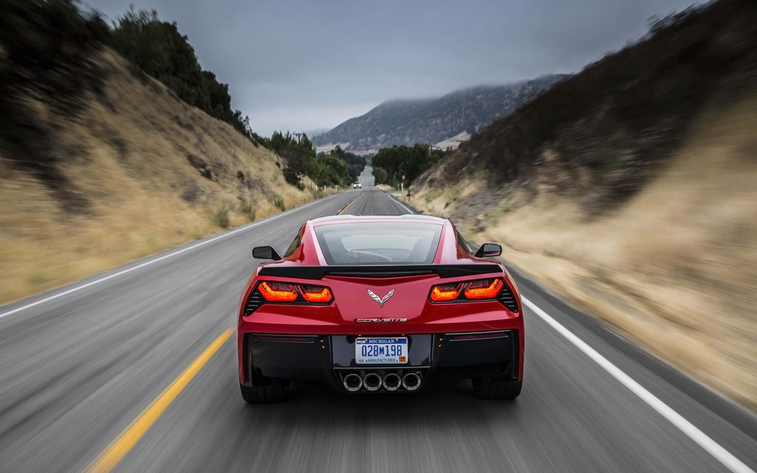 corvette 桌布 壁紙 — 一輛紅色Corvette跑車在蜿蜒的山路上疾駛，周圍環境模糊，天空多雲。