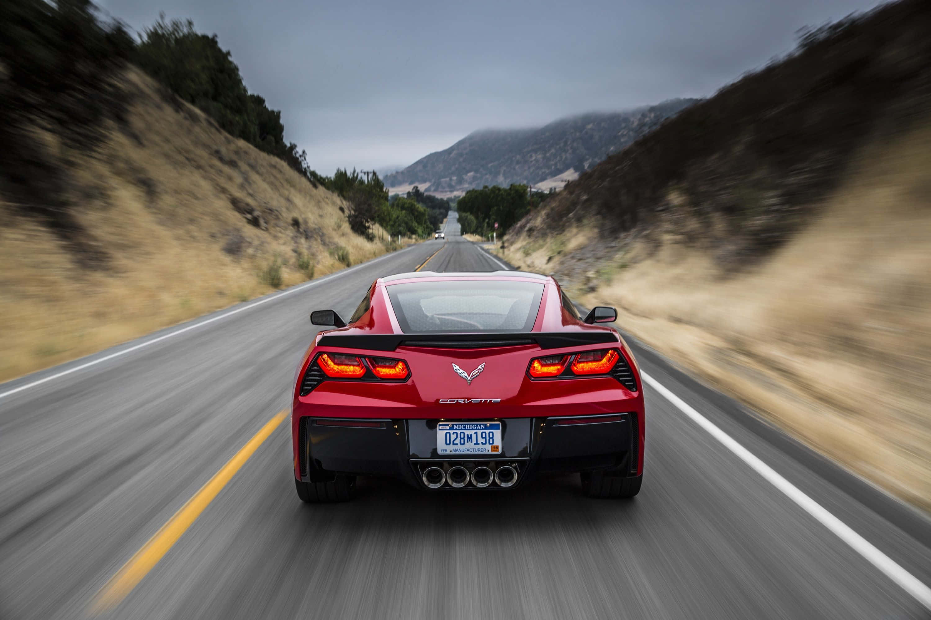 Chevrolet Corvette Stingray 桌布 壁紙 — 一輛紅色Corvette跑車在陰天下行駛於蜿蜒的山路上，周圍景物模糊。