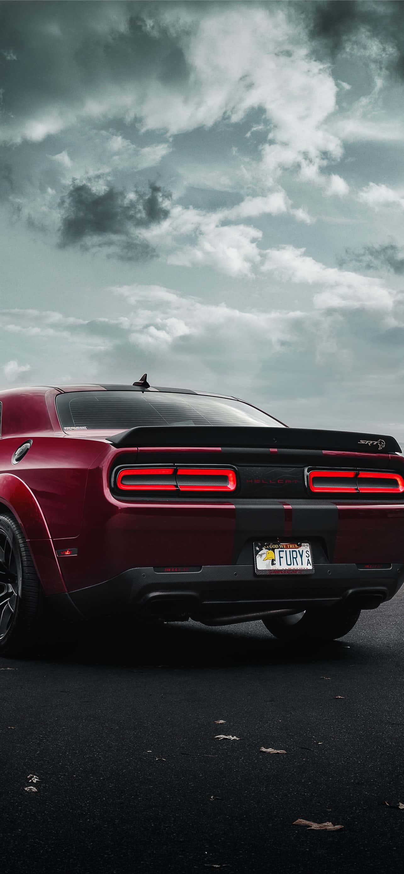 桌布 壁紙 — 一輛紅色Dodge Challenger Hellcat，亮著尾燈，停在戲劇性的多雲天空下濕漉漉的瀝青路上。