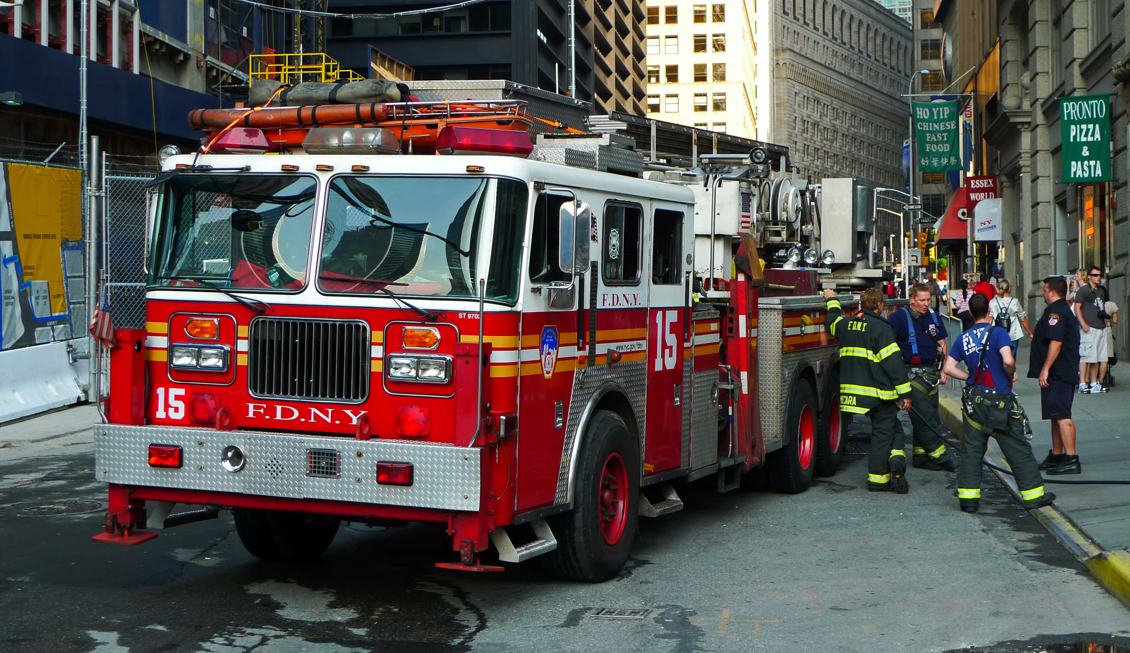 Fire Department 桌布 壁紙 — 一輛紅色FDNY消防車停放在濕漉漉的城市街道上，附近有消防員和旁觀者。