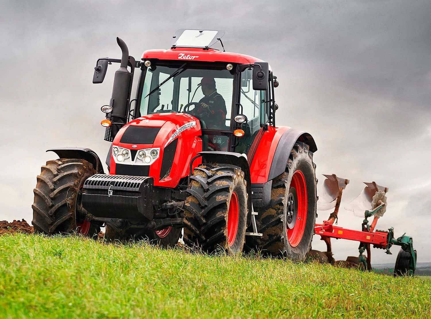 Tractor 桌布 壁紙 — 一輛紅色Fendt拖拉機，裝著沾滿泥巴的大輪胎，在陰天之下犁過鮮綠的草地。