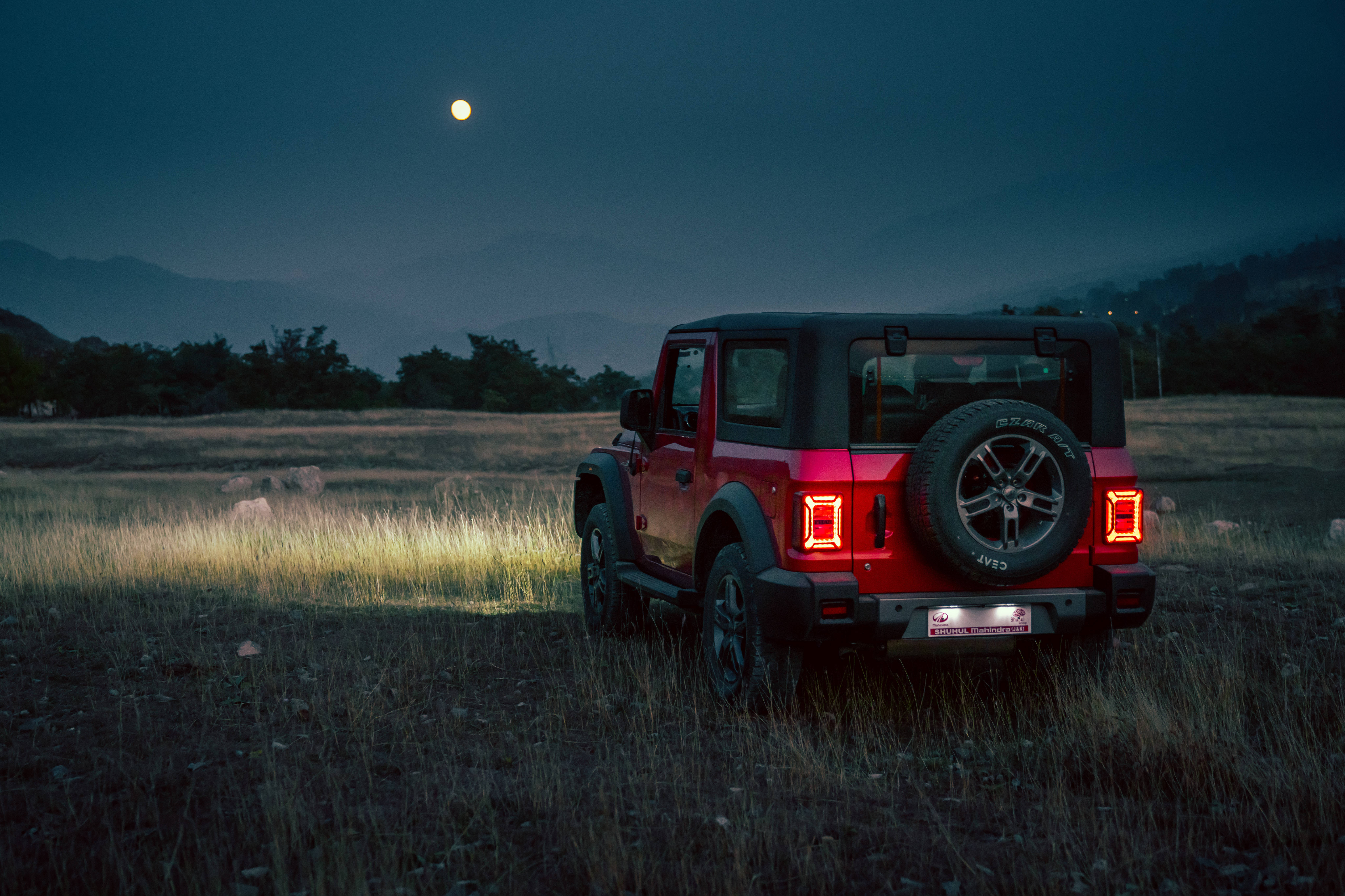 Moon Aesthetic 桌布 壁紙 — 一輛紅色Jeep Wrangler在黃昏時停泊在草地上，遠山之上掛著一輪滿月。