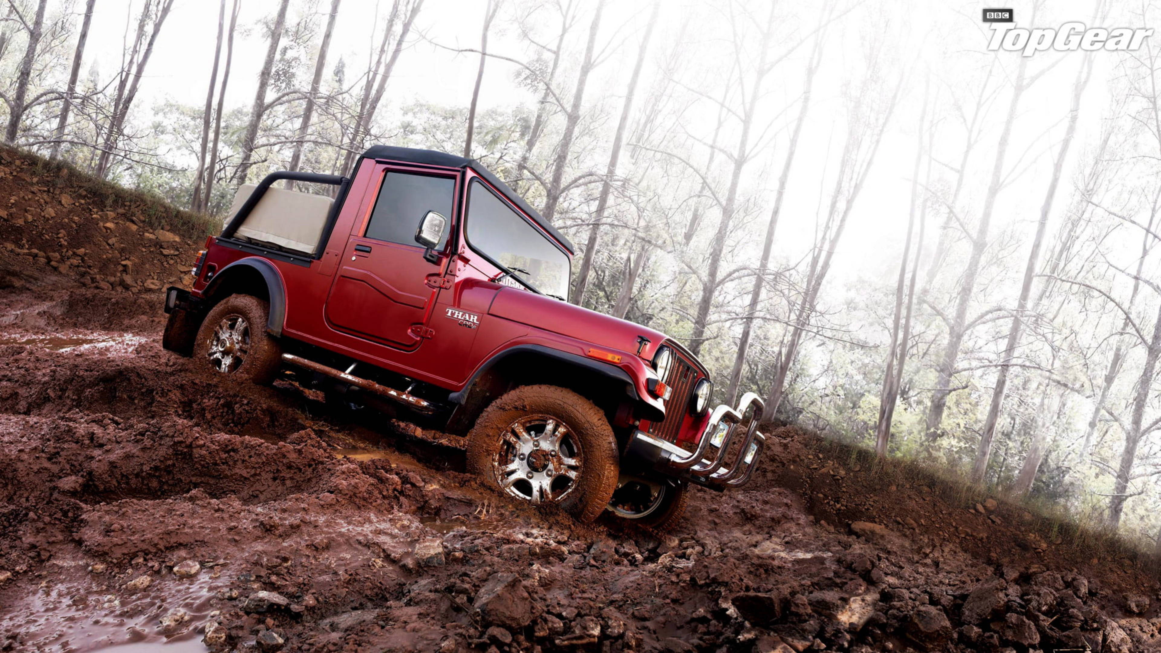 汽車 4K 桌布 壁紙 — 一輛紅色Mahindra Thar吉普車征服泥濘的森林小徑，堅固的輪胎在厚厚的棕色泥漿中旋轉。