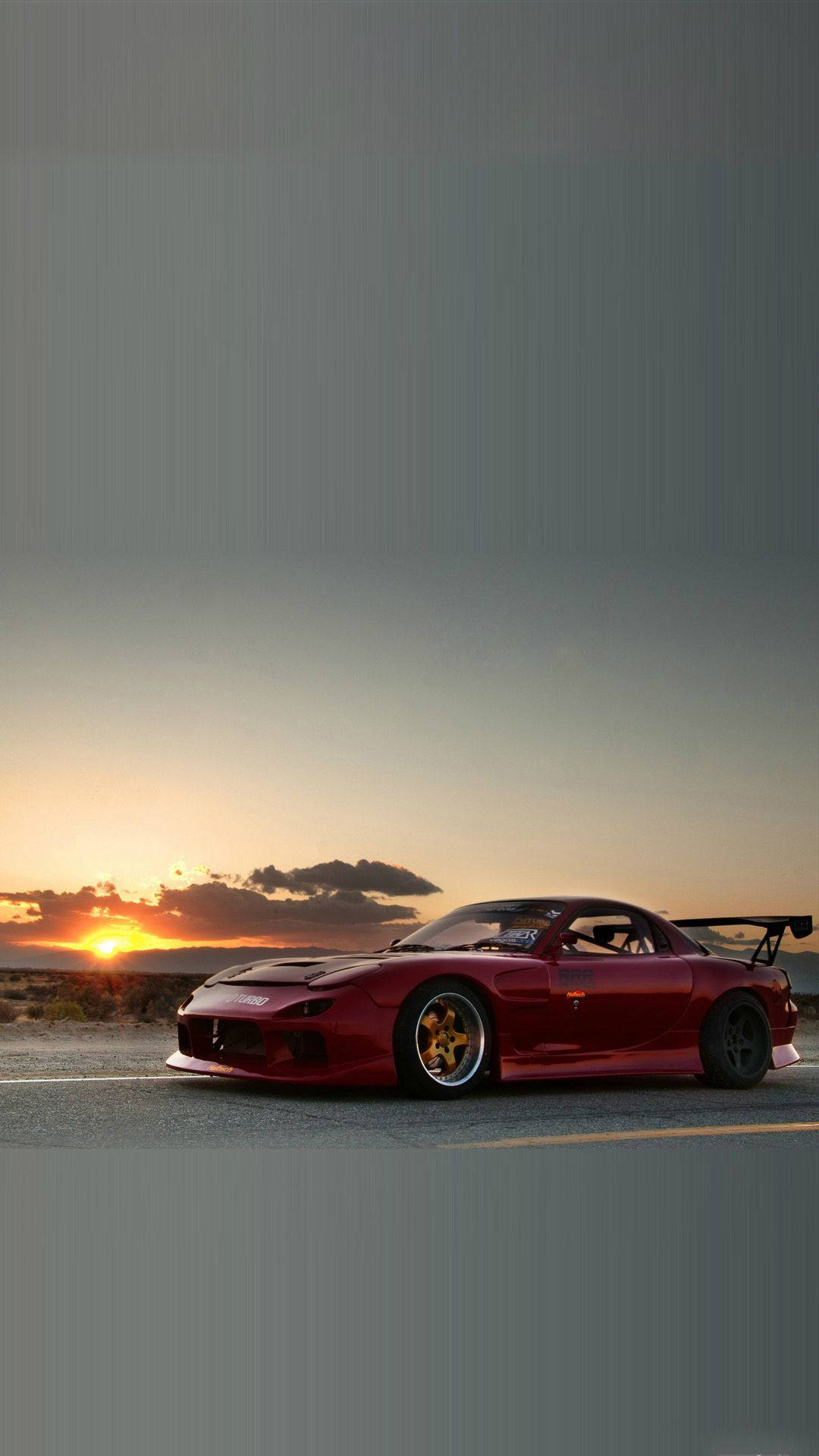Rx7 iPhone 桌布 壁紙 — 一輛紅色Mazda RX-7跑車配金色輪圈，停在沙漠公路上，夕陽西下，天空橙色，遠處有雲。