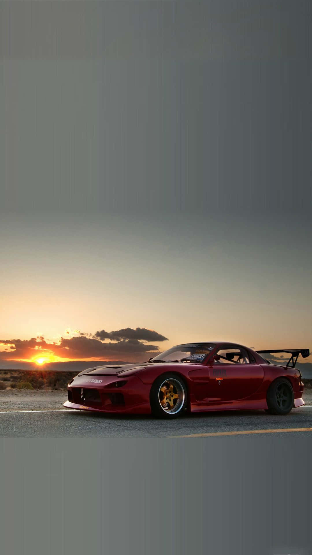 日落 桌布 壁紙 — 一輛紅色Mazda RX-7跑車配金色輪圈，停泊在日落時分空無一人的道路上，溫暖的橙色天空和遠處的雲朵。
