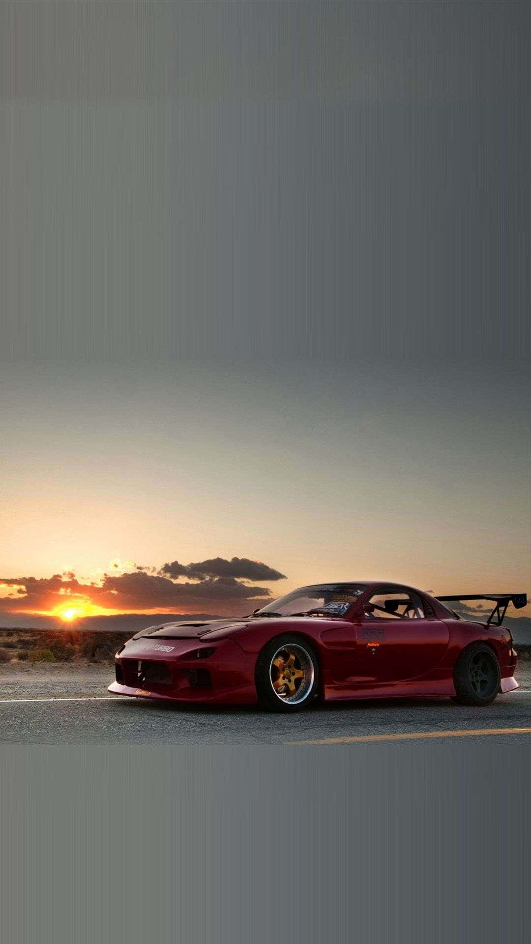 JDM 桌布 壁紙 — 一輛紅色Mazda RX-7跑車配金色輪圈，停在沙漠公路上，夕陽西下，溫暖的橙色天空。