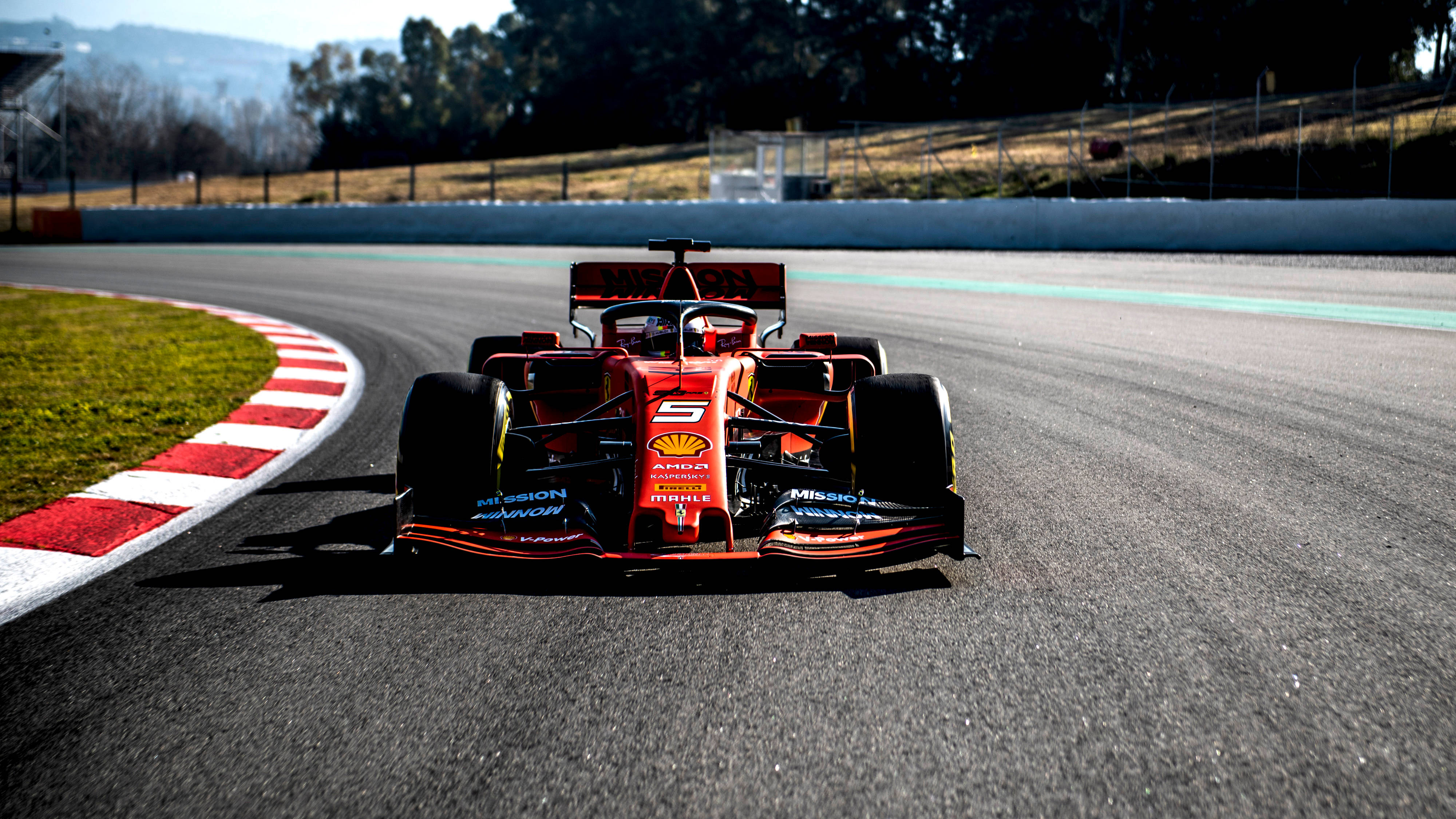 Formula 1 2019 桌布 壁紙 — 一輛紅色一級方程式賽車在明亮的日光下，在設有紅白路緣石的賽道彎道上高速行駛。