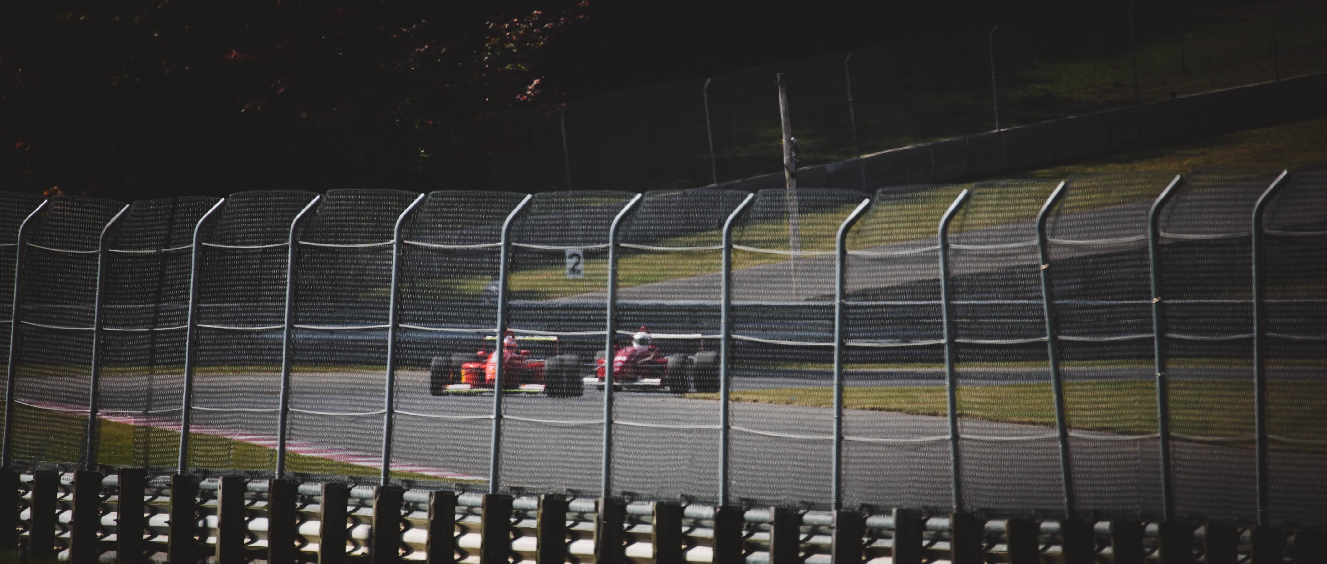 Racing 桌布 壁紙 — 一輛紅色一級方程式賽車在黃昏時分穿過安全圍欄，以模糊的動態沿著賽道飛馳。