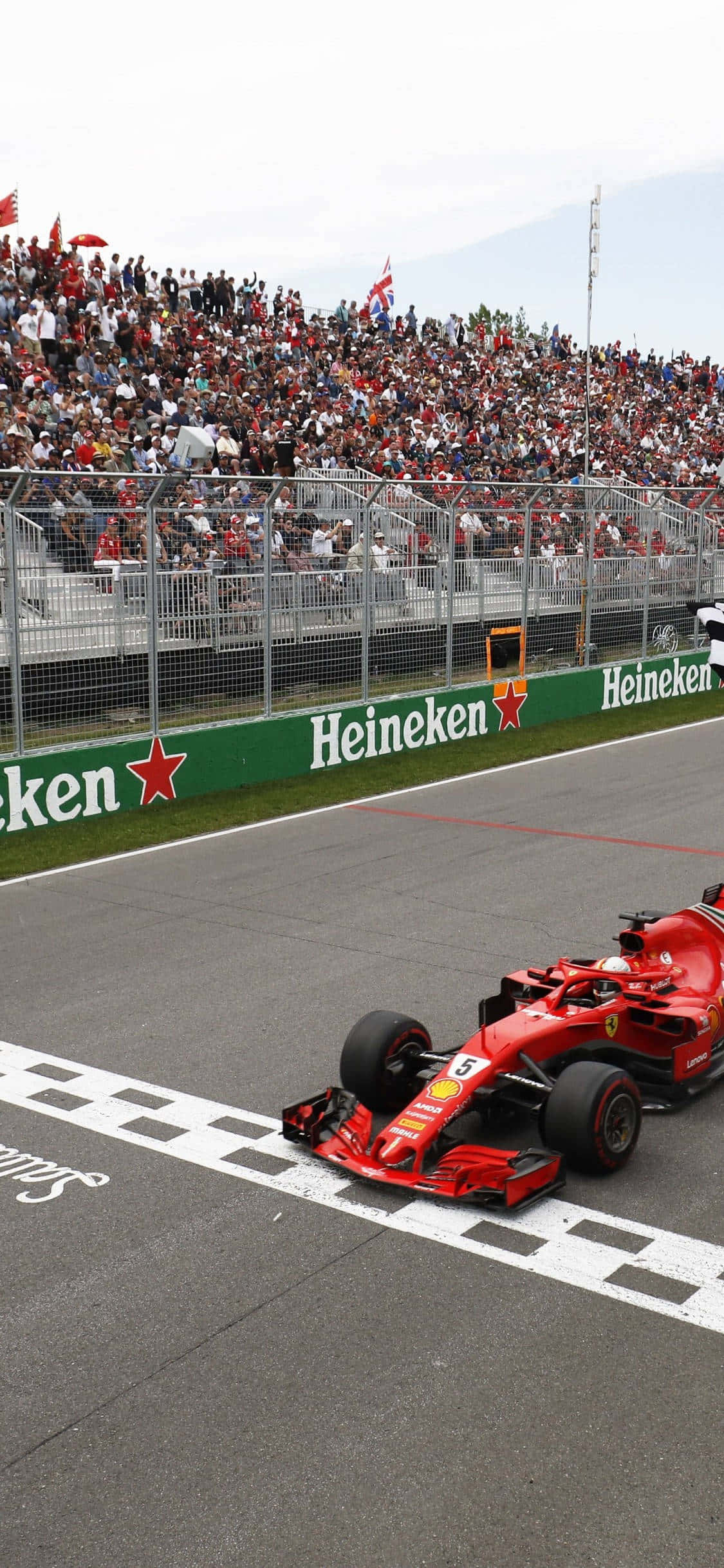 Formula 1 iPhone 桌布 壁紙 — 一輛紅色一級方程式賽車越過方格旗終點線，滿座的看台上傳來震耳欲聾的歡呼聲。