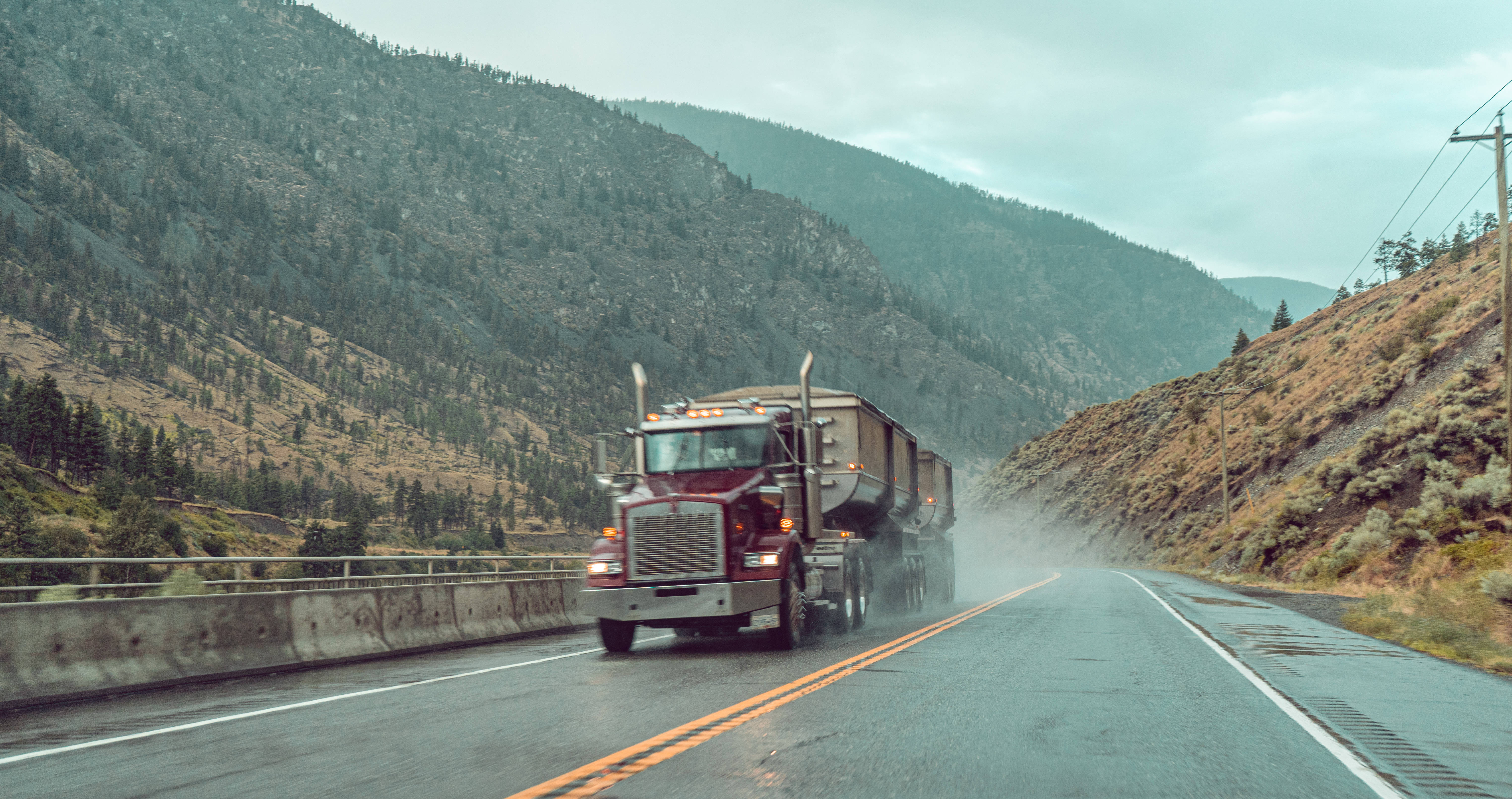 Truck 桌布 壁紙 — 一輛紅色半掛卡車在陰天下行駛在潮濕的山區高速公路上運載貨物。