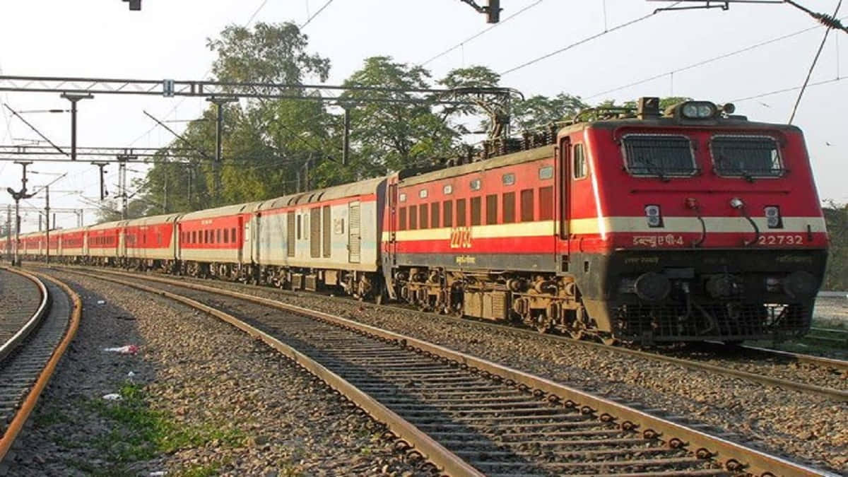 Indian Railway 桌布 壁紙 — 一輛紅色和奶油色的印度鐵路電力機車在黃金時段沿著彎曲的軌道穿過綠色樹線拉動客運列車。