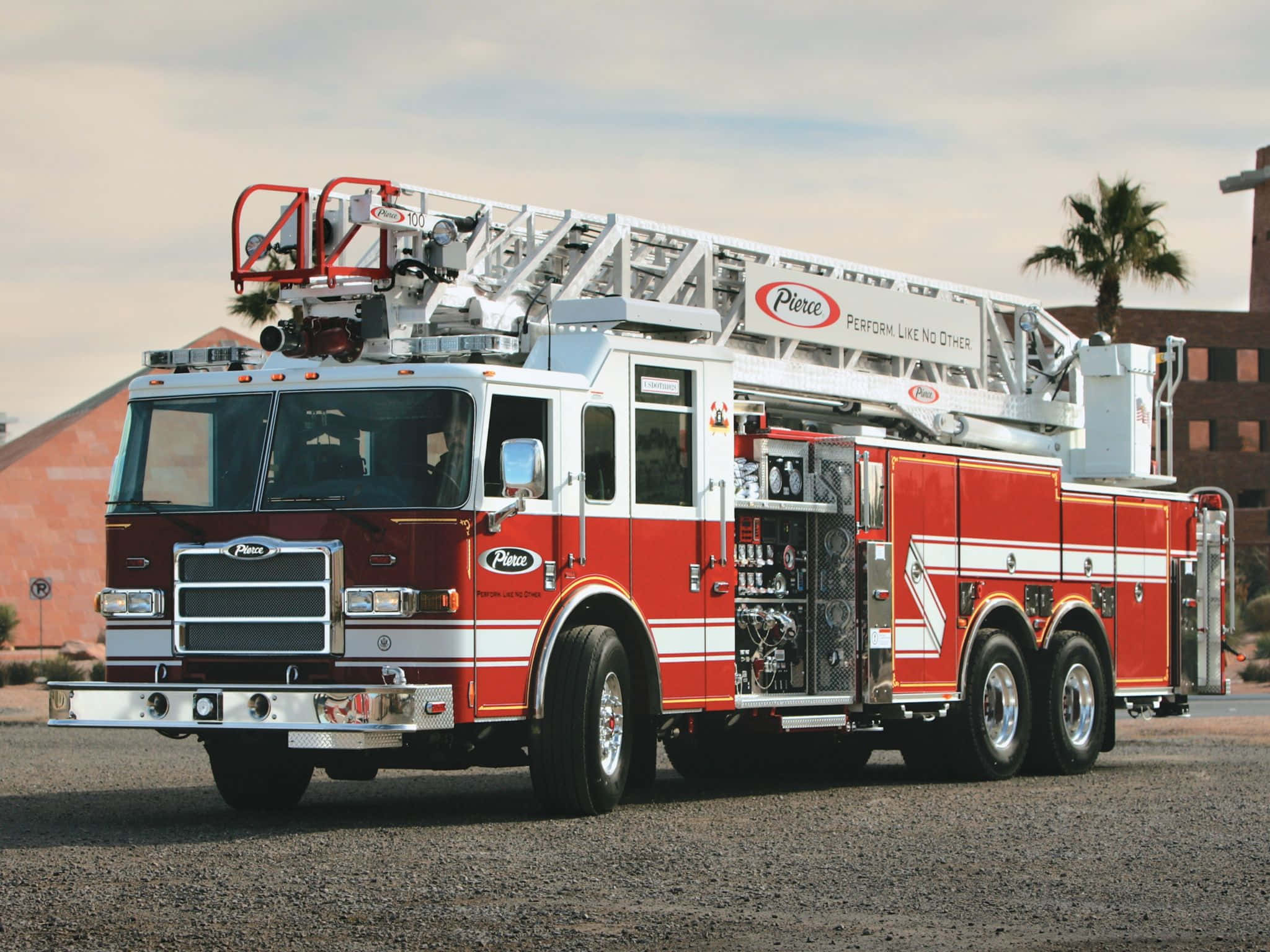 Fire Truck 桌布 壁紙 — 一輛紅色和白色的 Pierce 消防車，梯子已伸展，停放在建築物附近的碎石地上，天空朦朧。