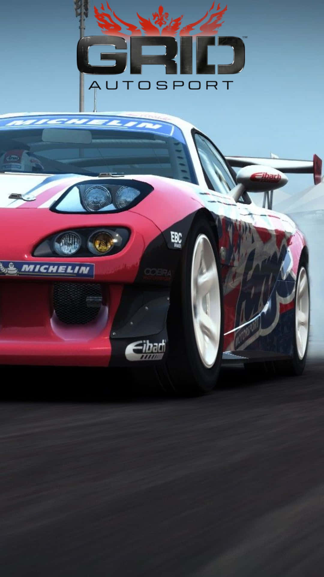 Grid Autosport 桌布 壁紙 — 一輛紅色和藍色的賽車在晴朗的天空下，以動態模糊效果和可見的贊助商標誌在賽道上飛馳。