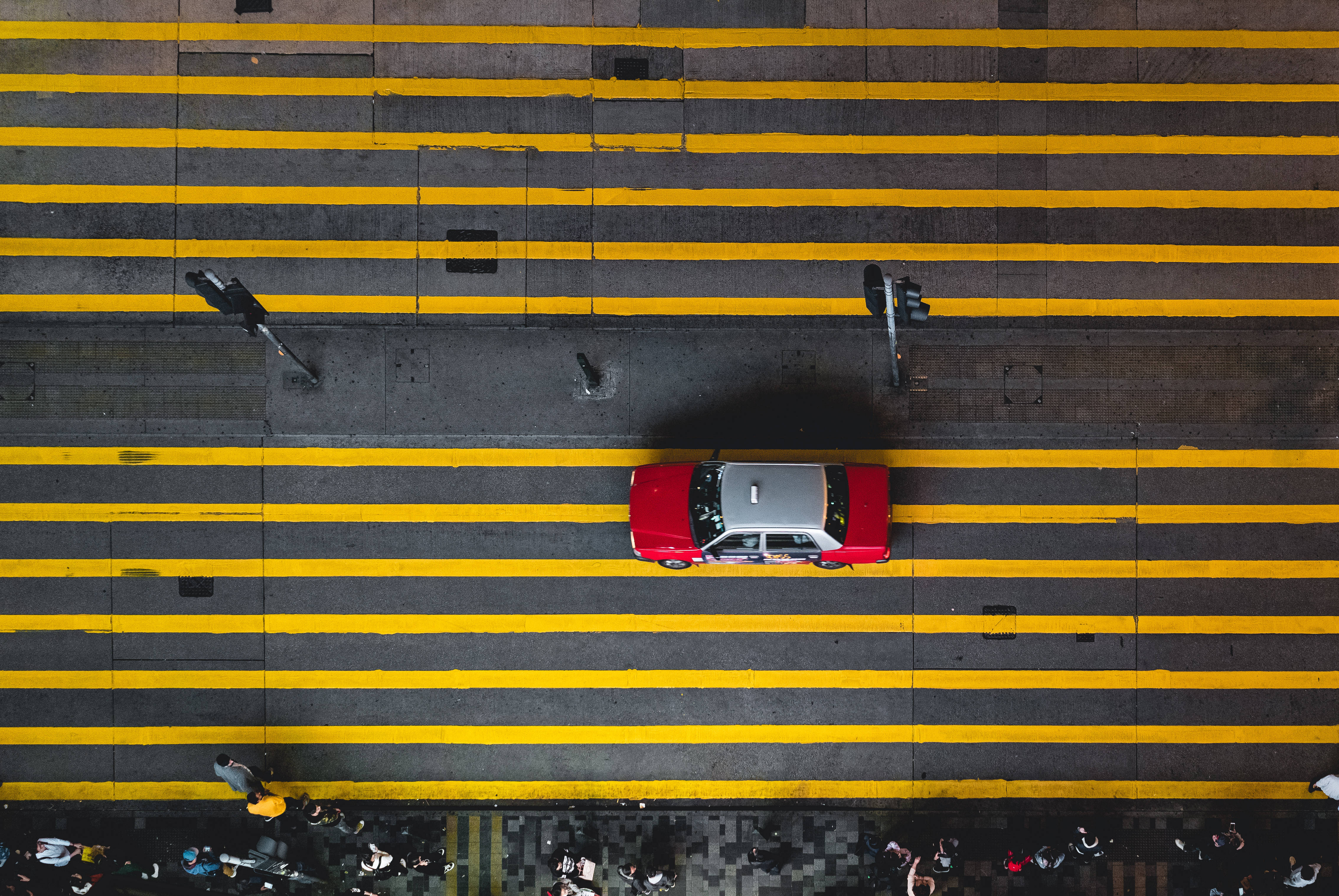 香港 桌布 壁紙 — 一輛紅色和銀色的計程車從俯視角度駛過城市街道上大膽的黃色條紋。