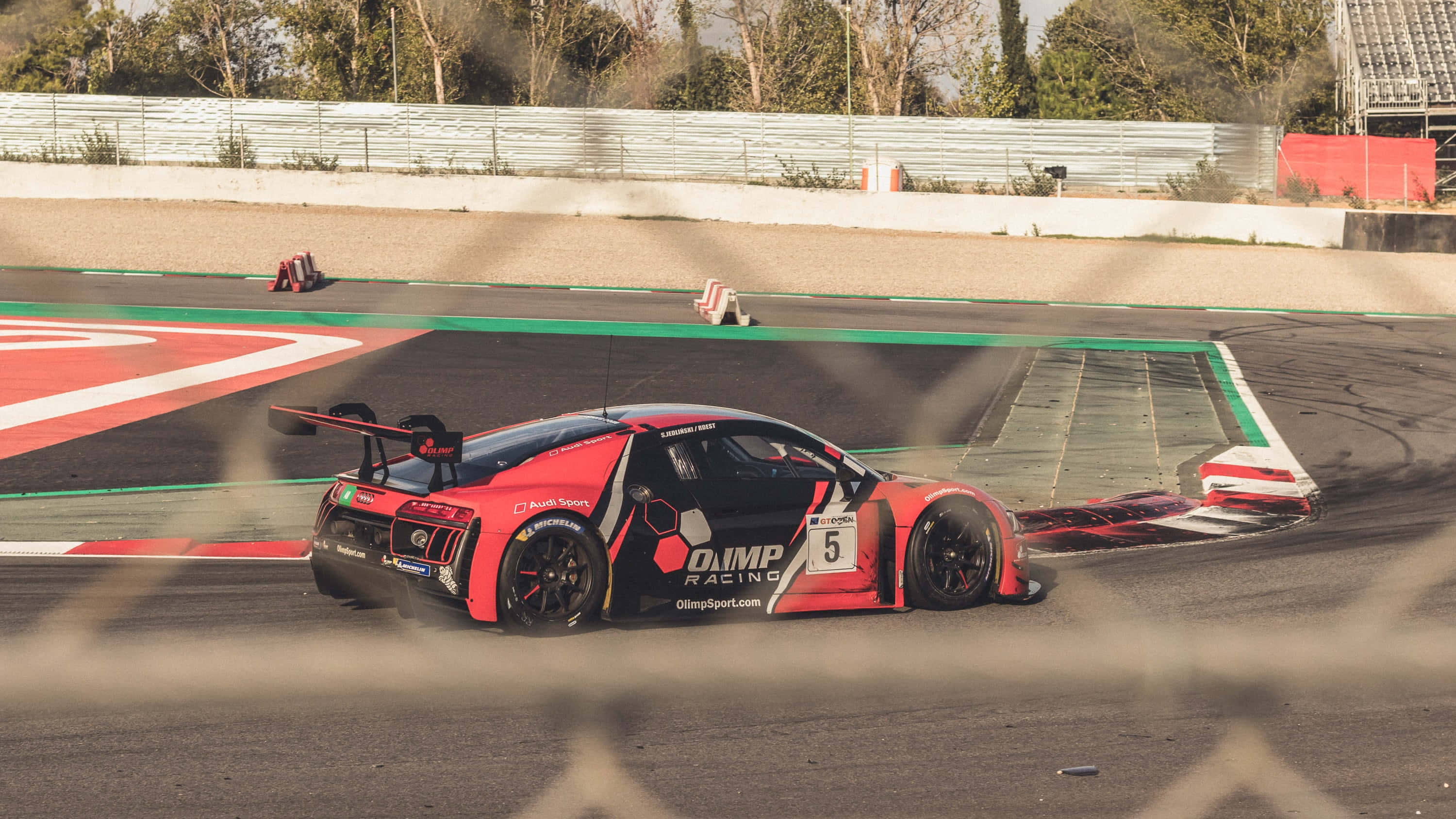 Race Track 桌布 壁紙 — 一輛紅色和黑色、編號5的賽車在明亮的日光下於賽道彎道飄移，揚起煙霧。