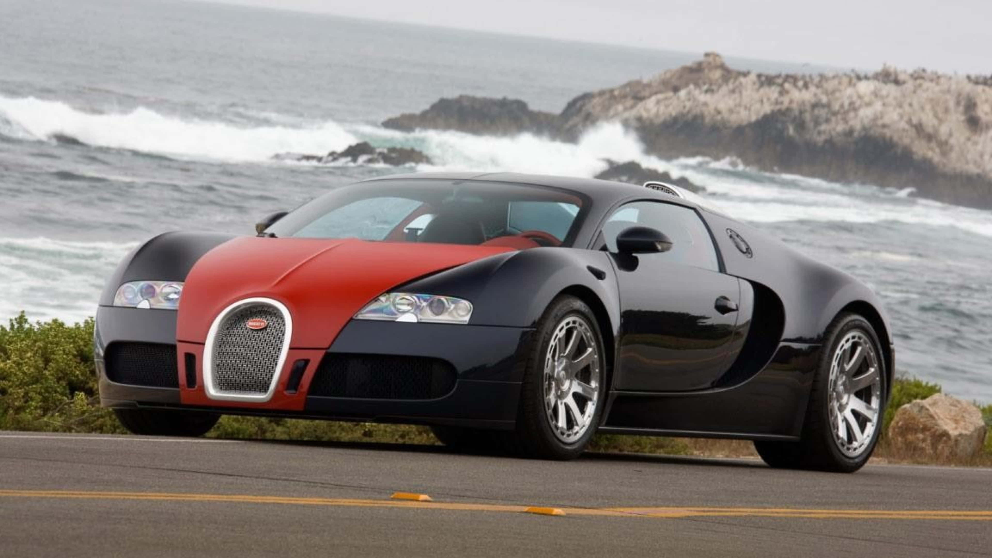 bugatti iPhone 桌布 壁紙 — 一輛紅色和黑色的布加迪威龍停泊在沿海公路上，背景是洶湧的海浪和岩石峭壁。