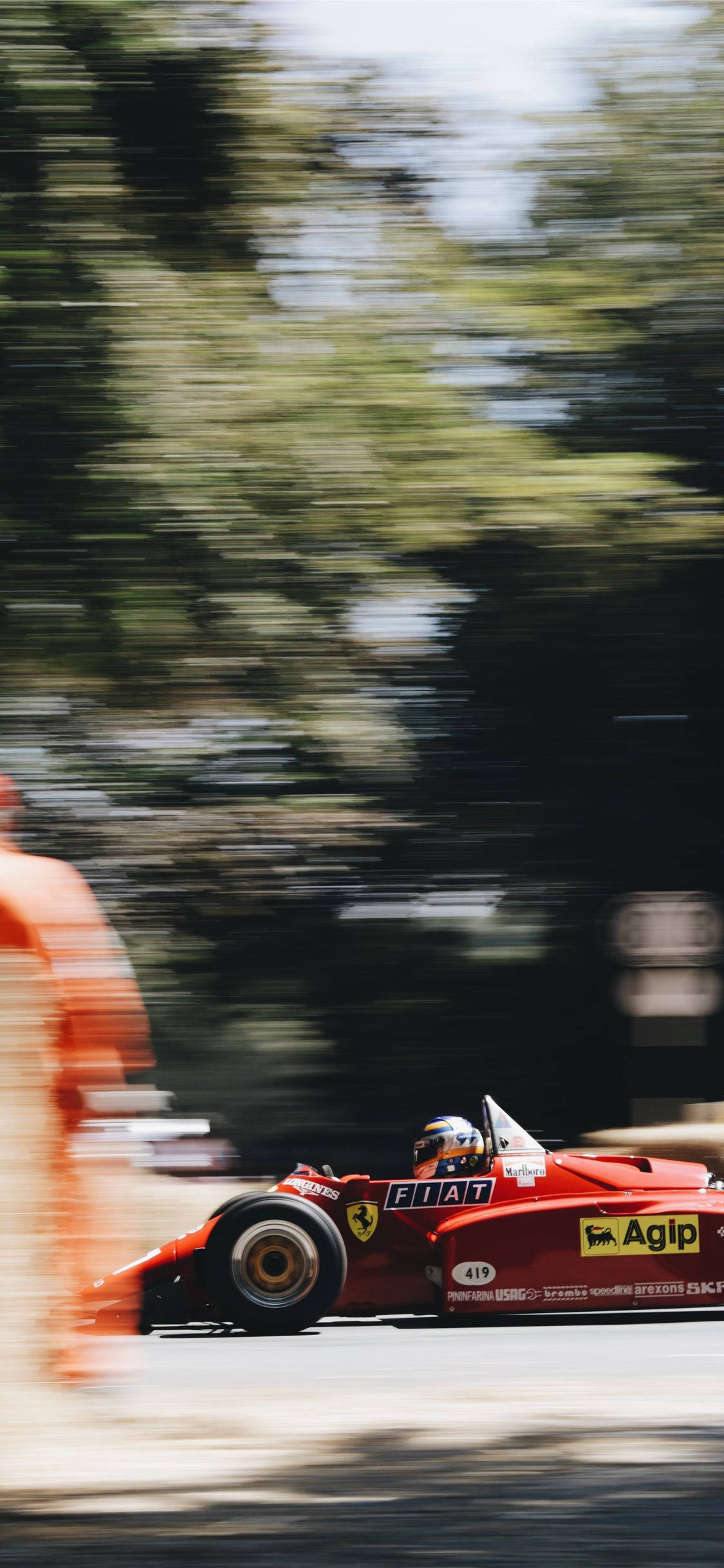 F1 iPhone 壁紙 桌布 壁紙 — 一輛紅色復古賽車在高速賽道活動中模糊地掠過樹木和觀眾。