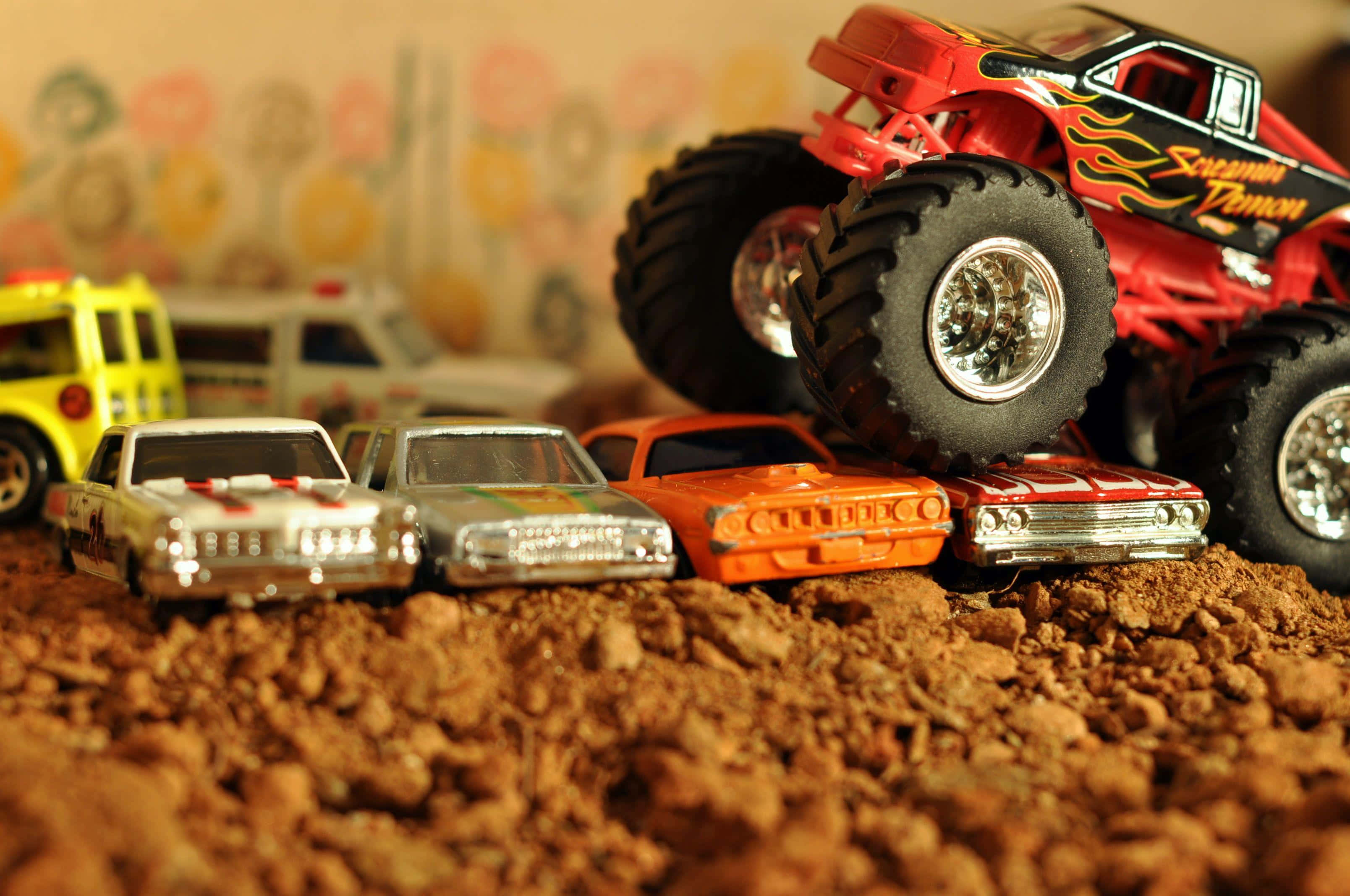 Monster Truck 桌布 壁紙 — 一輛紅色怪獸卡車聳立在一排復古玩具車之上，背景是 gritty 的泥土表面和花卉壁紙。