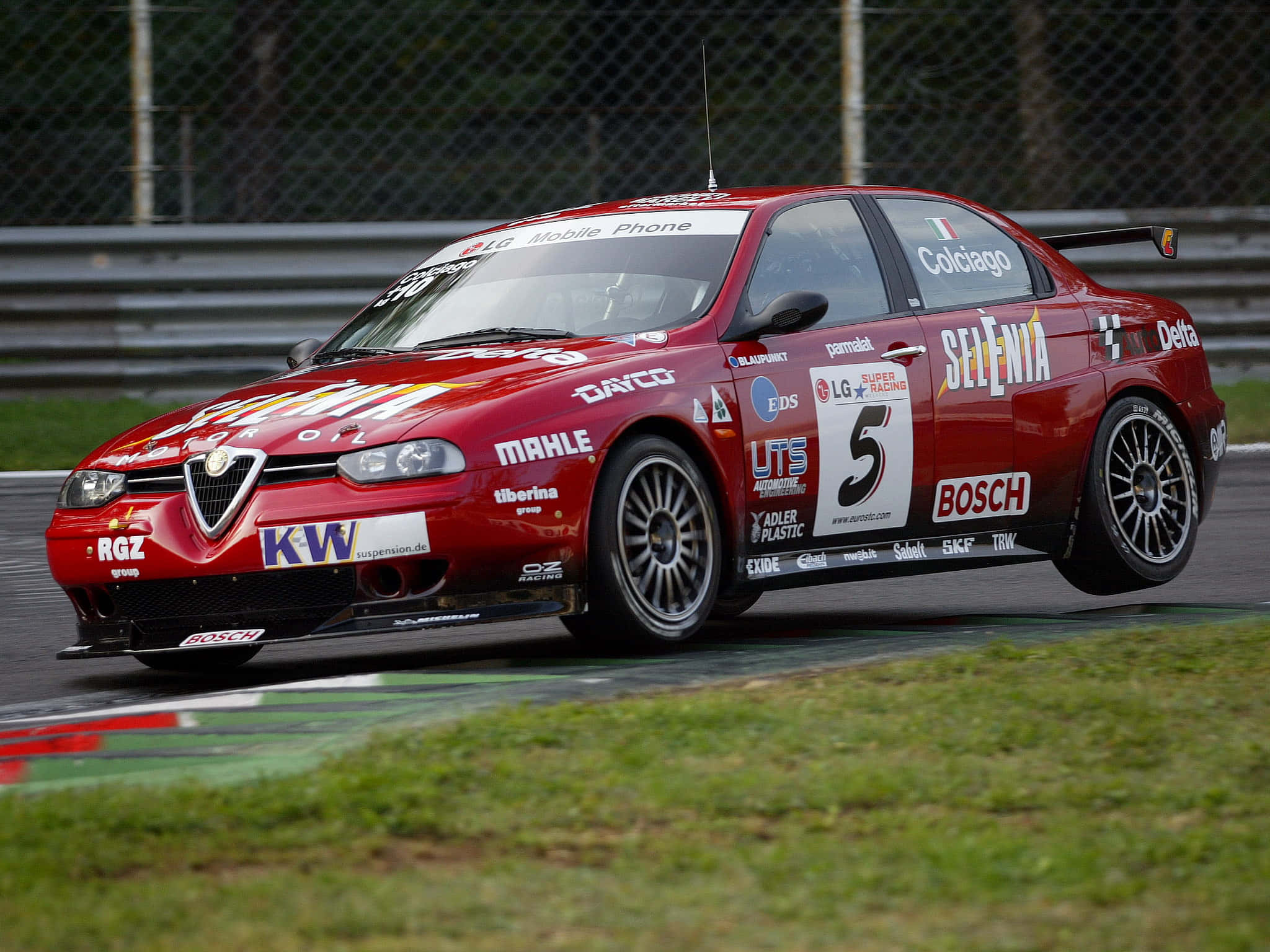 Alfa Romeo 156 桌布 壁紙 — 一輛紅色愛快羅密歐賽車（編號5）在潮濕的賽道上疾馳，賽道兩旁是綠色草地和安全護欄。