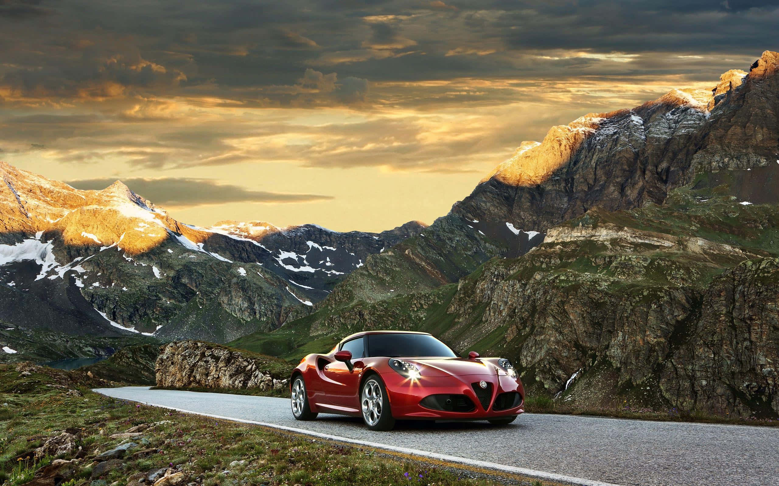 Alfa Romeo 4c 桌布 壁紙 — 一輛紅色愛快羅密歐跑車在戲劇性的金色日落天空下行駛在蜿蜒的山路上。