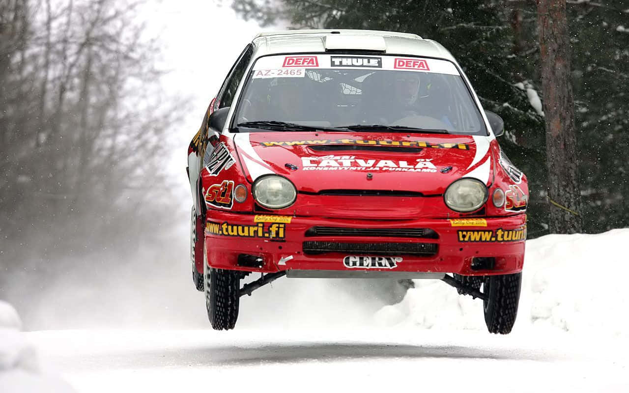 Ice Racing 桌布 壁紙 — 一輛紅色拉力賽車在雪地森林中飛躍，在冬季比賽中激起雪霧。