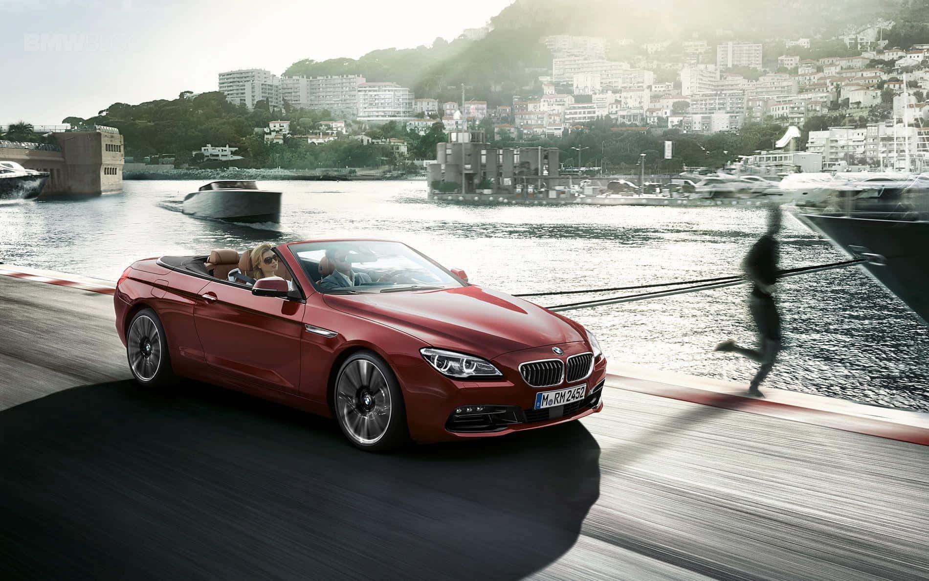Bmw 6 Series 桌布 壁紙 — 一輛紅色敞篷寶馬在海濱道路上疾馳，背景中有一個模糊的跑者和遊艇碼頭。