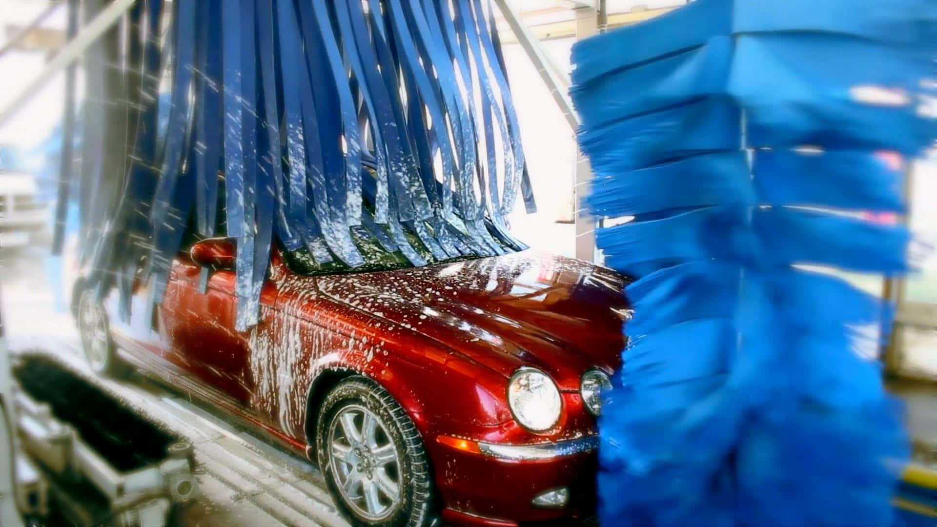 洗車 桌布 壁紙 — 一輛紅色汽車正在自動洗車機中被藍色刷子大力清洗，水花四濺。