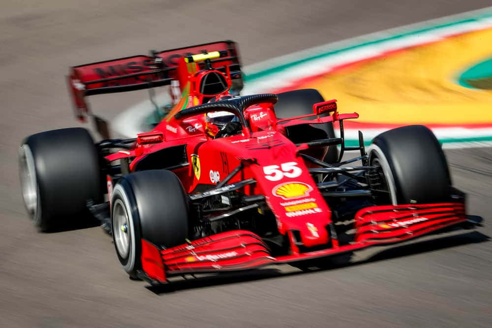 F1 桌布 壁紙 — 一輛紅色法拉利F1賽車，車號55，在賽道上高速奔馳，帶有動態模糊和彩色路緣。