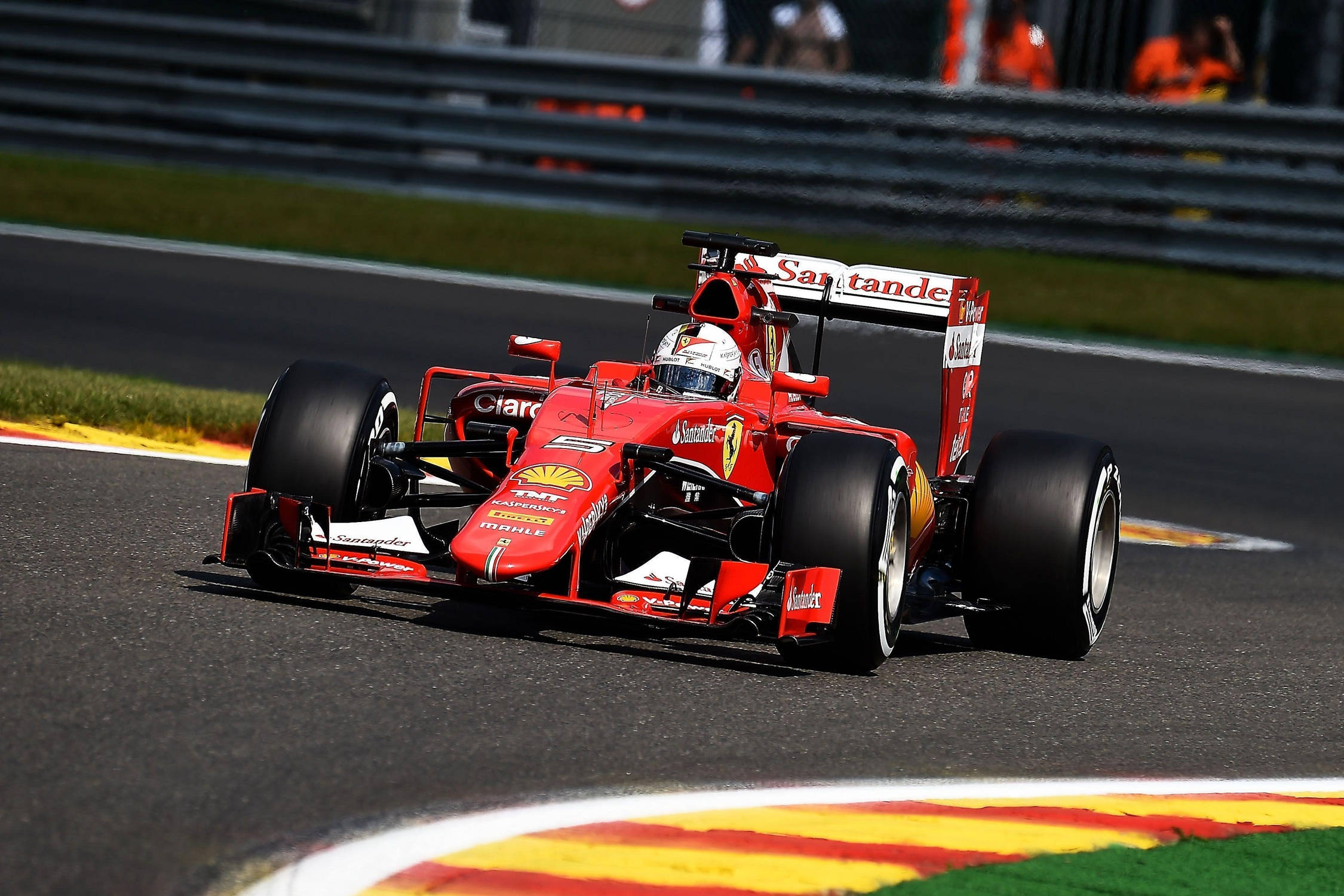Formula 1 Desktop 桌布 壁紙 — 一輛紅色法拉利F1賽車在明亮的日光下，沿著賽道彎道高速行駛，彎道設有鮮豔的黃色和紅色路緣石。
