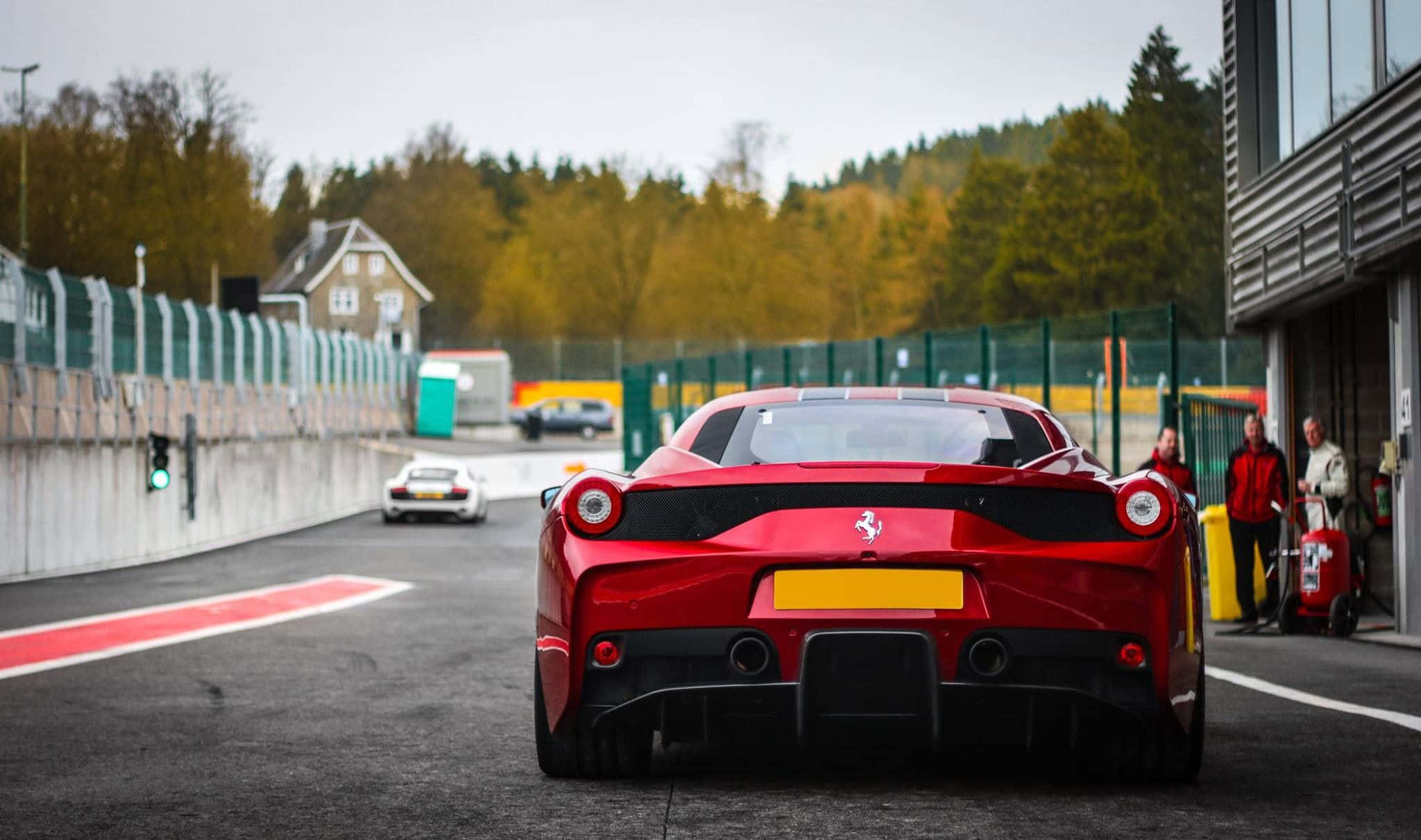 Ferrari 458 Speciale 桌布 壁紙 — 一輛紅色法拉利LaFerrari停在賽道入口，背景有秋樹和現代車庫。
