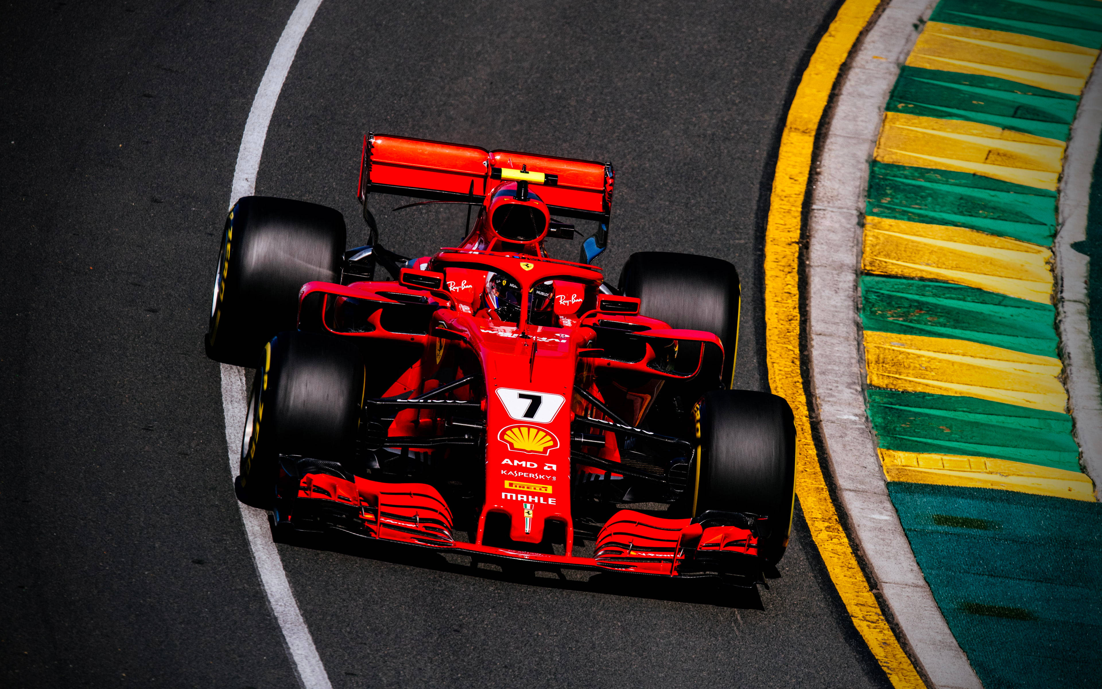 ferrari f1 2018 桌布 壁紙 — 一輛紅色法拉利一級方程式賽車，車號7，在彎曲的瀝青賽道上緊貼著黃色和綠色的路緣石飛馳。