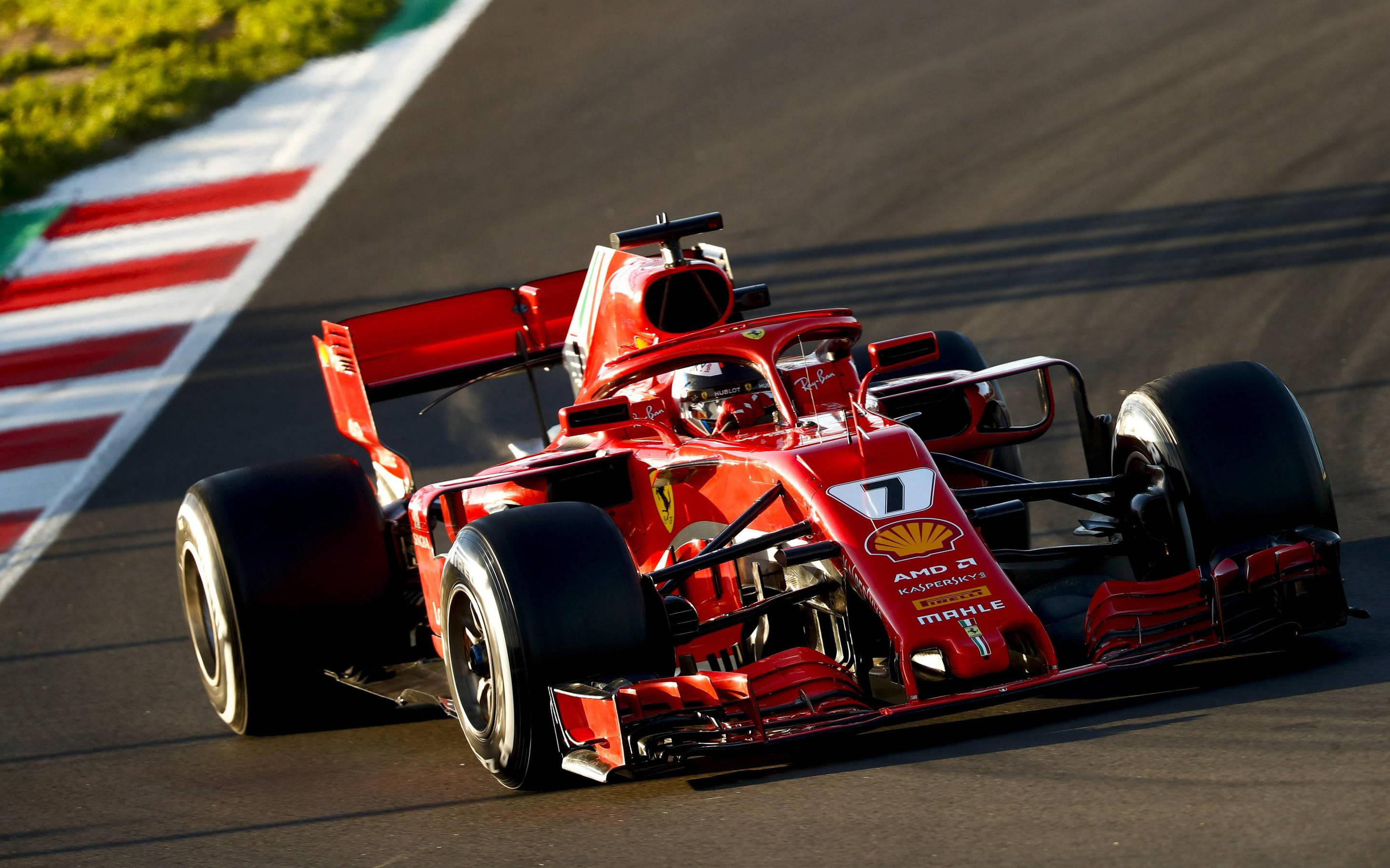 ferrari f1 2018 桌布 壁紙 — 一輛紅色法拉利一級方程式賽車，車號7，在陽光普照的賽道上奔馳，賽道邊緣有紅、白、綠三色路肩。