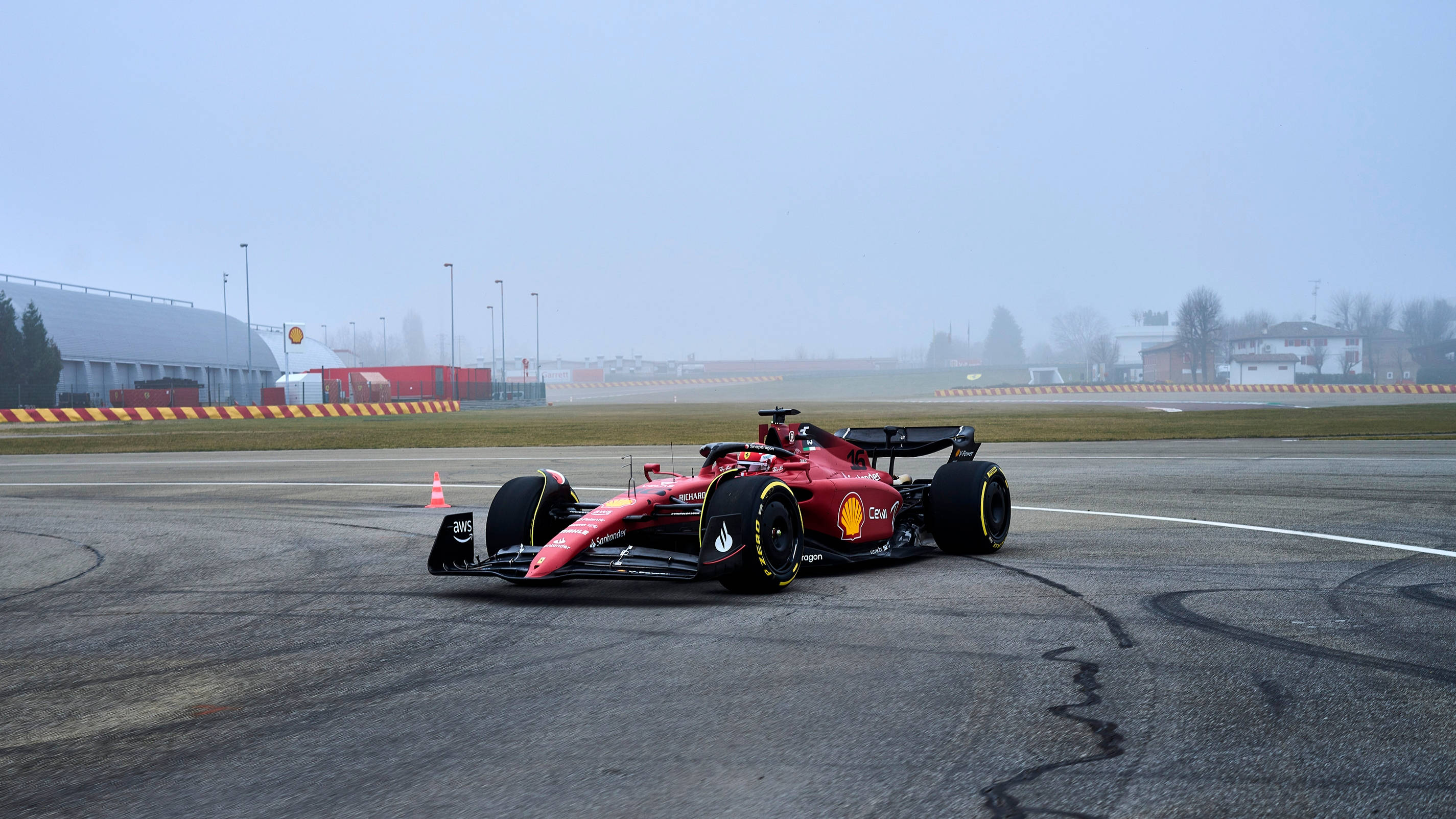 Formula 1 Desktop 桌布 壁紙 — 一輛紅色法拉利一級方程式賽車在多雲的天空下，在潮濕的賽道彎道上飄移，輪胎煙霧尾隨其後。