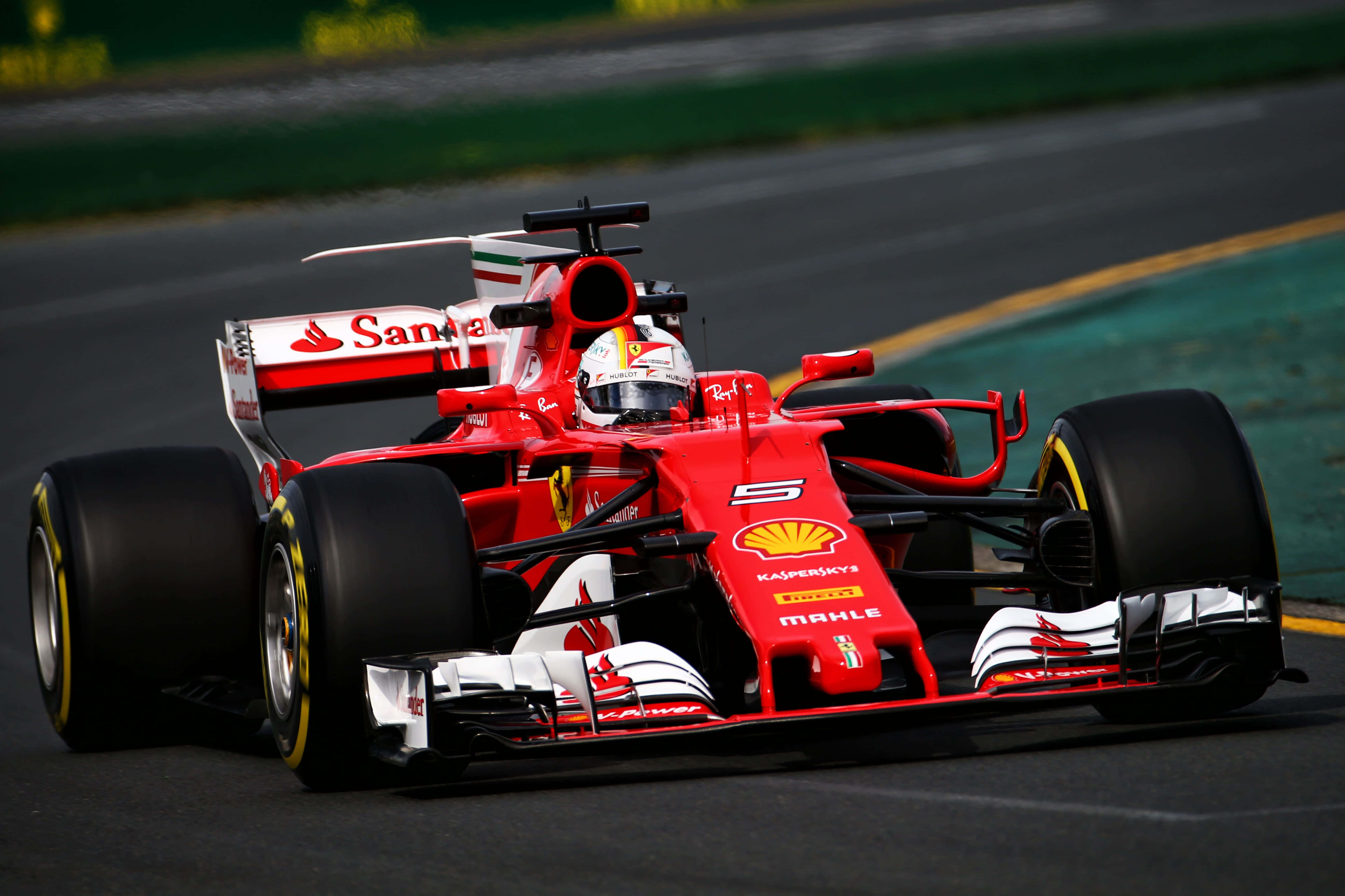Max Verstappen 桌布 壁紙 — 一輛紅色法拉利一級方程式賽車在賽道上奔馳，賽道上有綠色草地和黃色路緣。