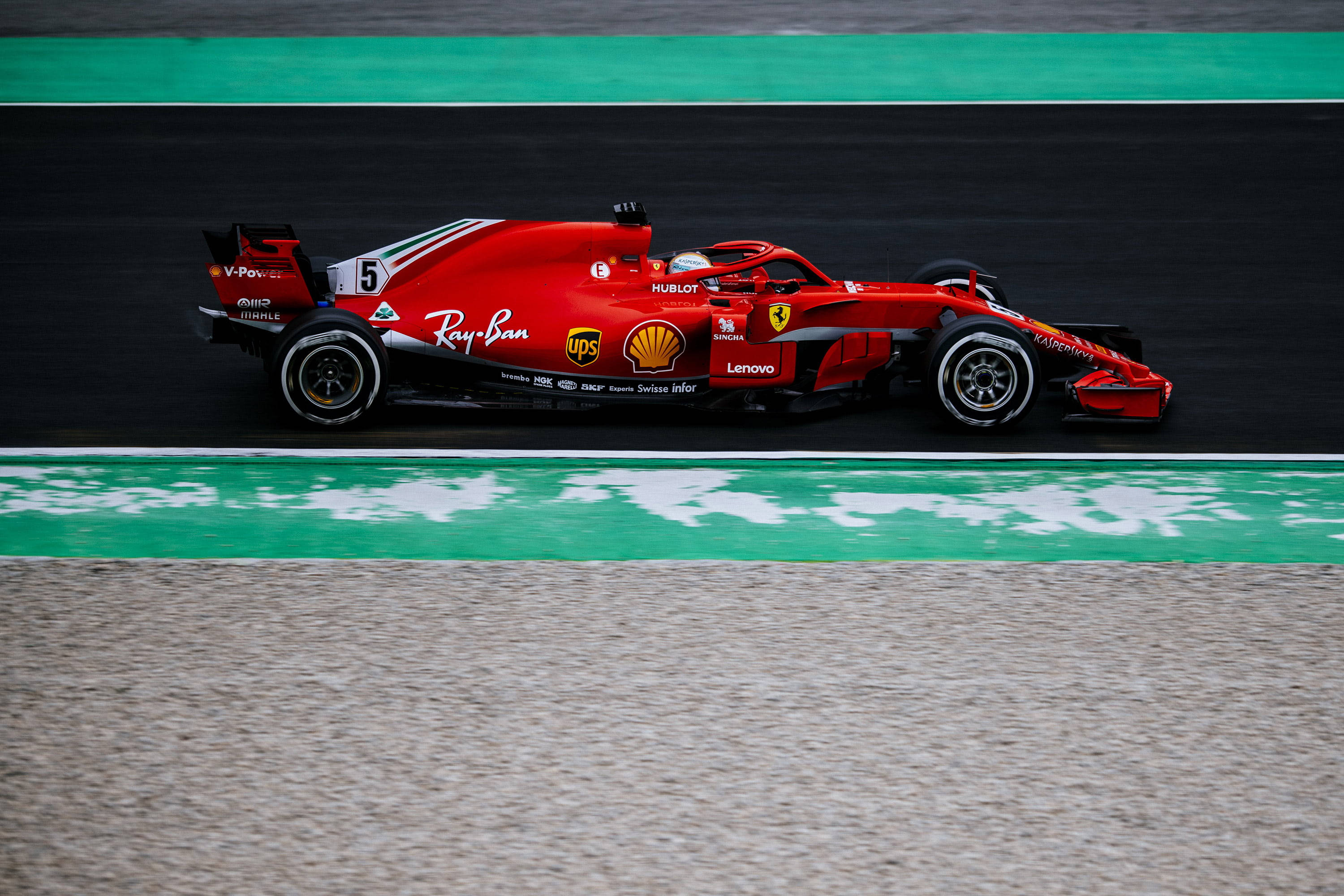 ferrari f1 2018 桌布 壁紙 — 一輛紅色法拉利一級方程式賽車沿著由綠色路緣和碎石包圍的賽道飛馳。
