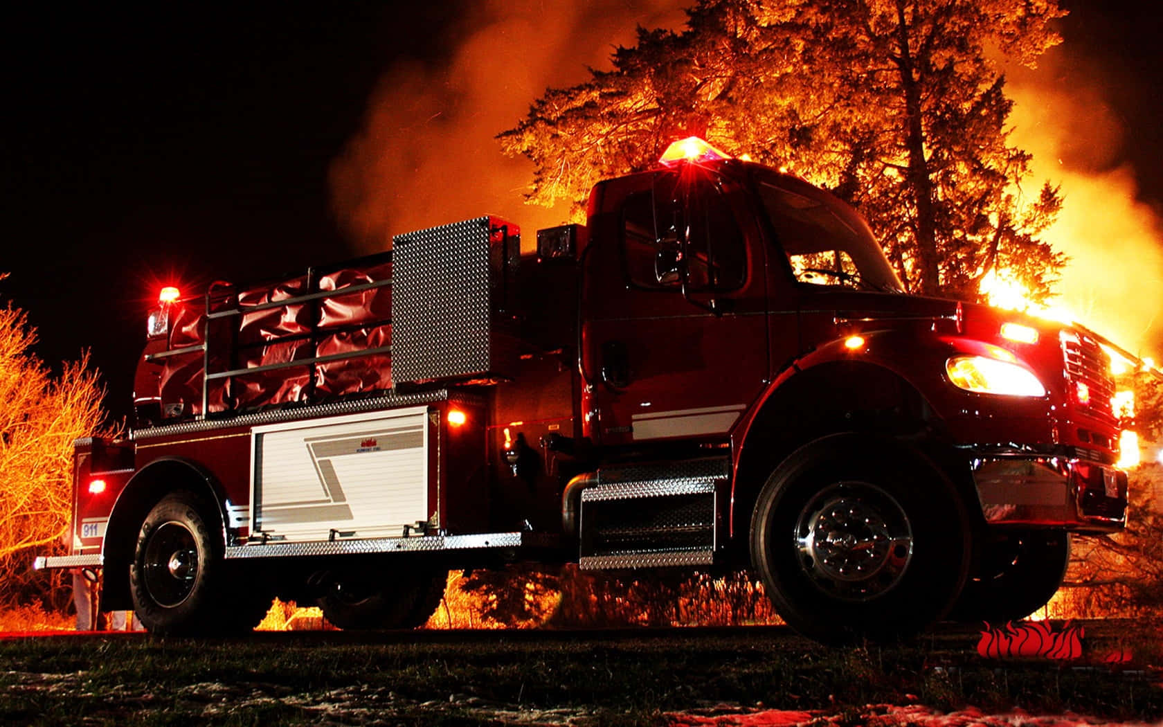 Fire Truck 桌布 壁紙 — 一輛紅色消防車在夜間準備就緒，背後火焰和煙霧升騰，照亮樹木和設備。