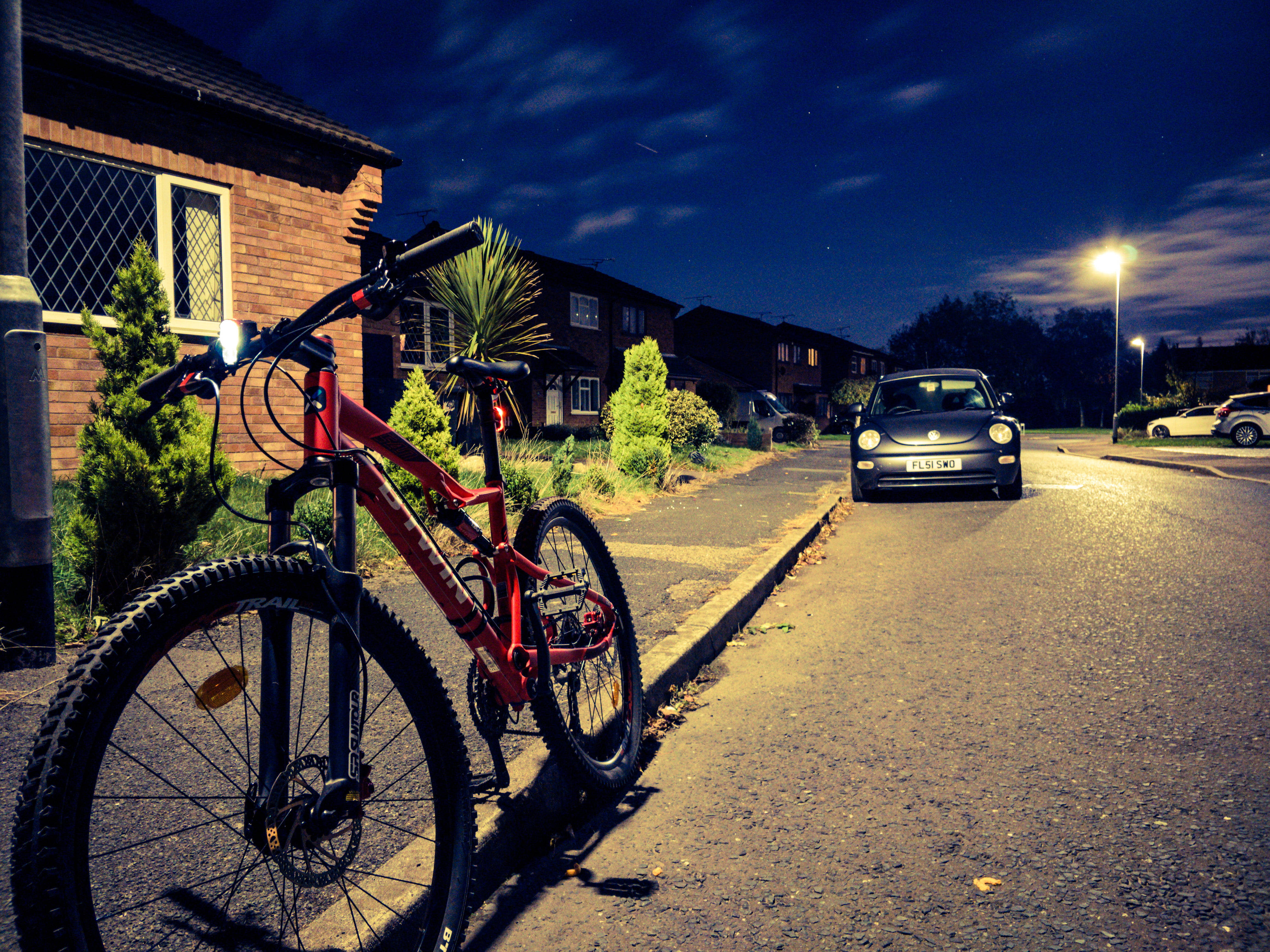 Mountain Bike 桌布 壁紙 — 一輛紅色登山車在星空下的寧靜住宅區夜晚靠著路邊，附近停著一輛復古汽車。