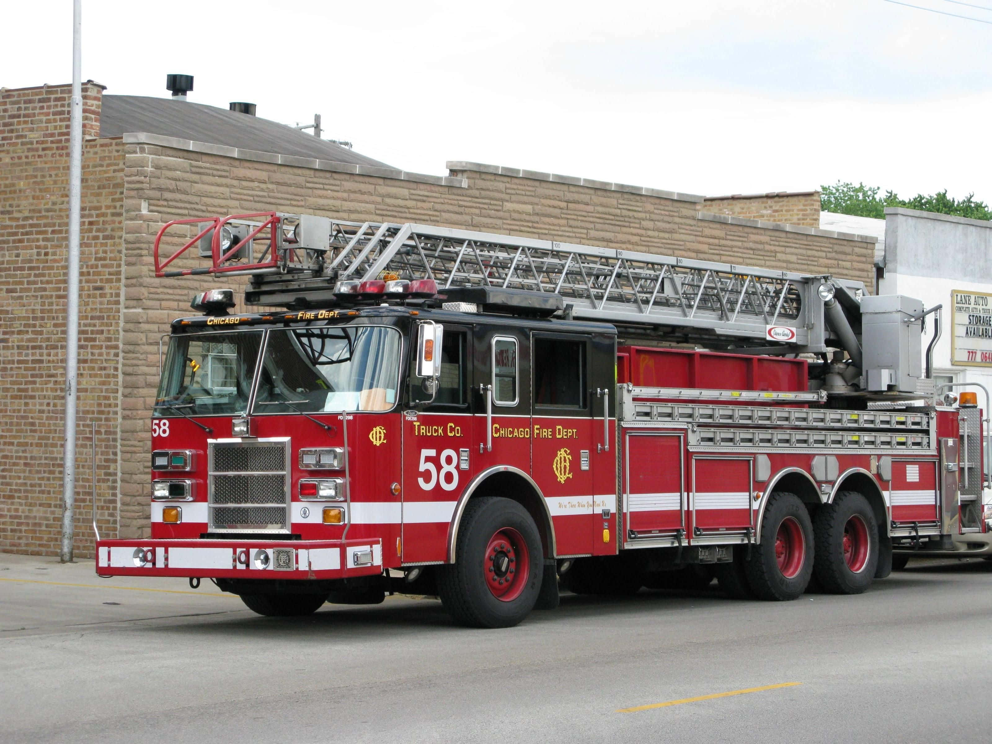 Fire Truck 桌布 壁紙 — 一輛紅色的芝加哥消防局雲梯車停泊在磚造建築旁的街道上，天空多雲。