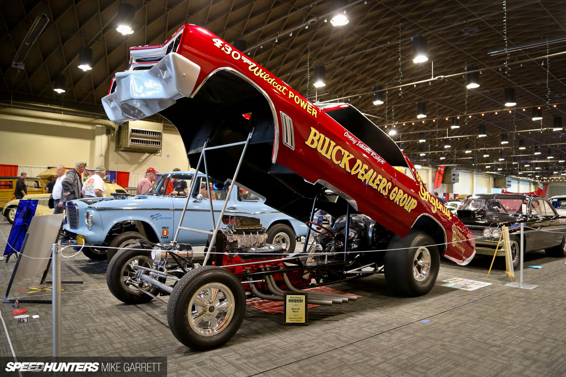 cars 桌布 壁紙 — 一輛紅色直線加速賽車，上面有「430 Wildcat Power」和「Buick Dealers Group」字樣，在室內車展中打開引擎蓋展示引擎。