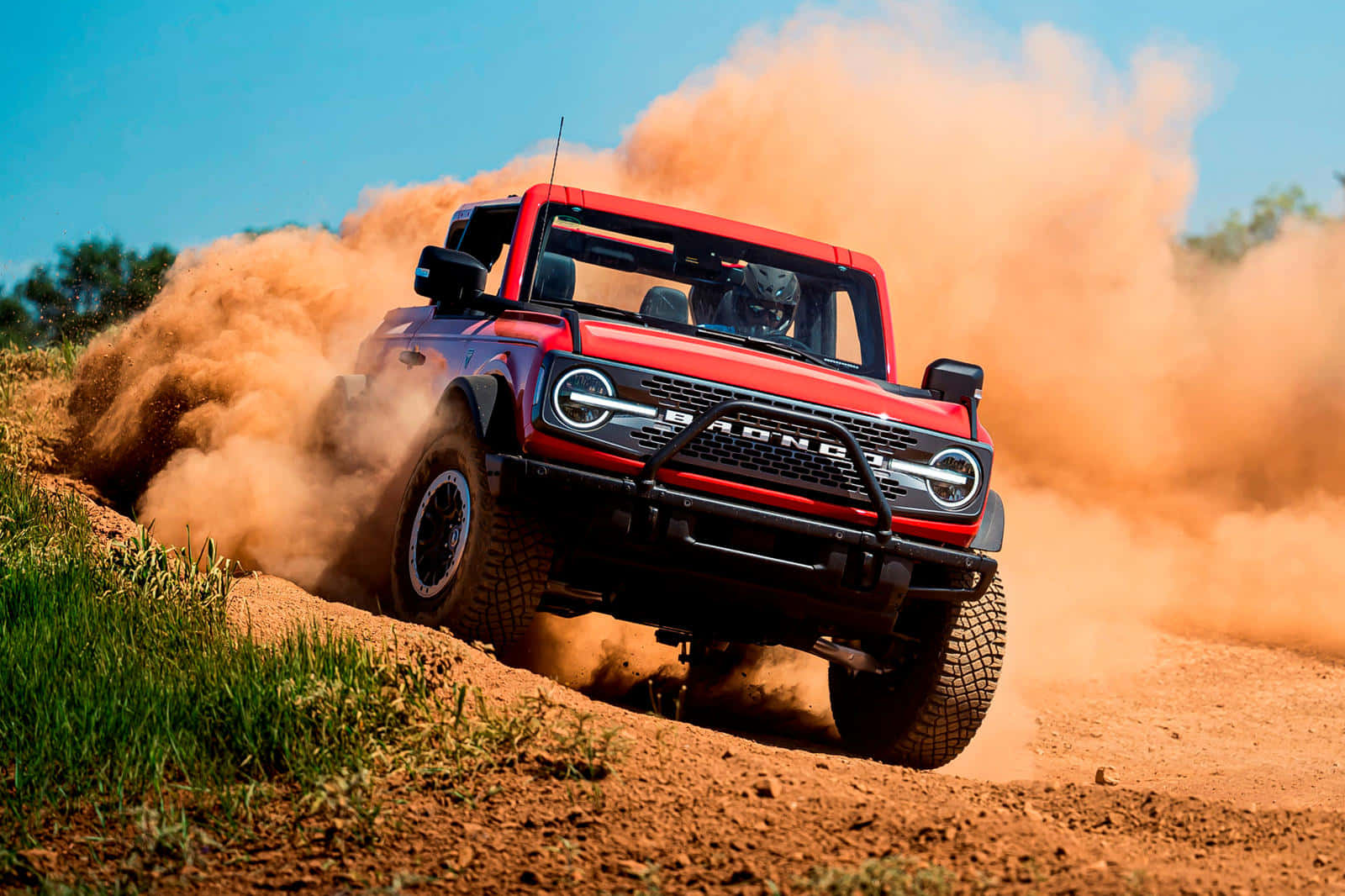 Ford Bronco 桌布 壁紙 — 一輛紅色福特 Bronco Raptor 在晴朗的藍天下咆哮著駛上塵土飛揚的泥土山坡，揚起巨大的橙色塵雲。