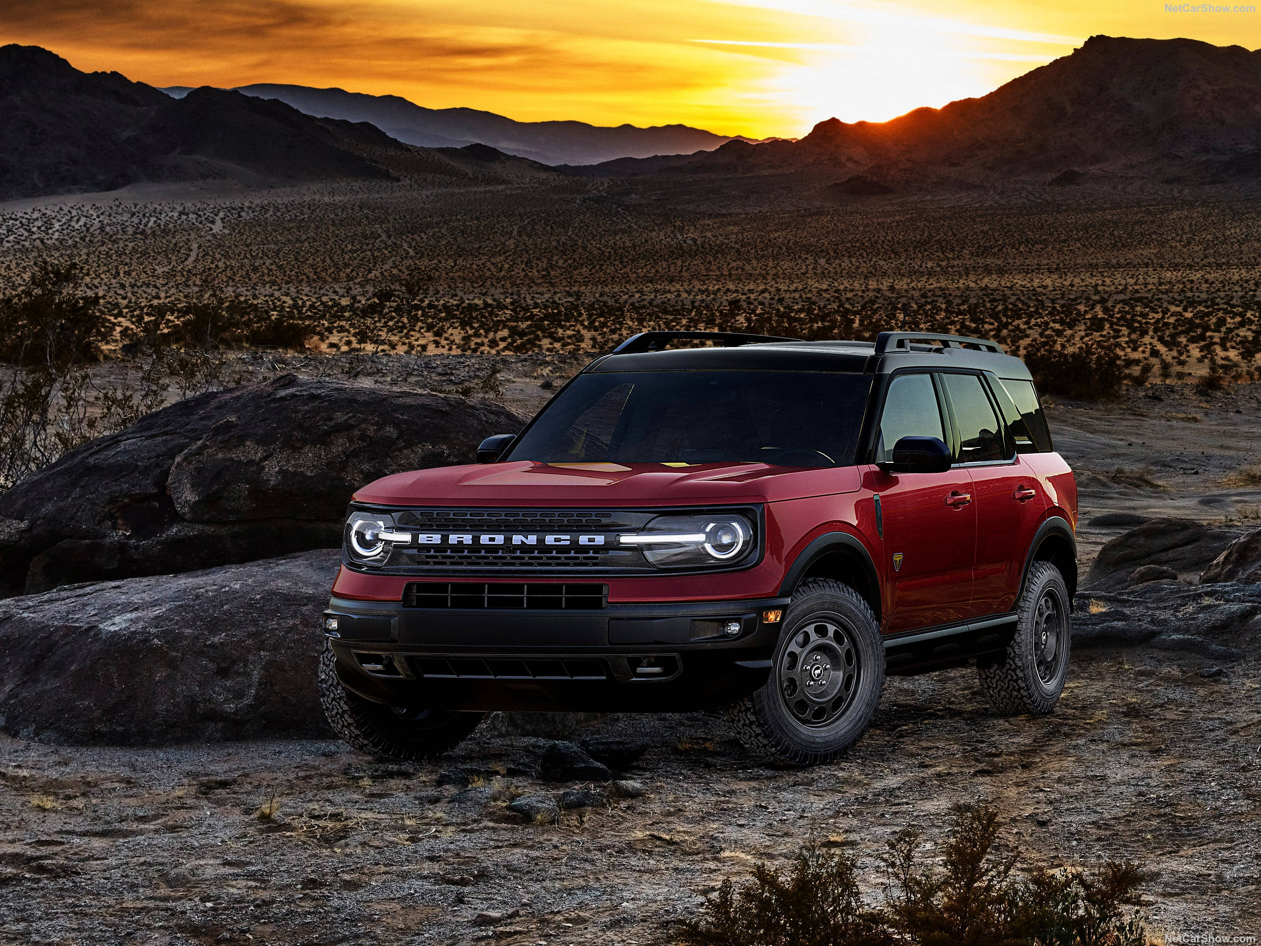 Ford Bronco 桌布 壁紙 — 一輛紅色福特Bronco SUV在日落時分的沙漠中傲然矗立，金色的光線在岩石地形上投下長長的陰影。