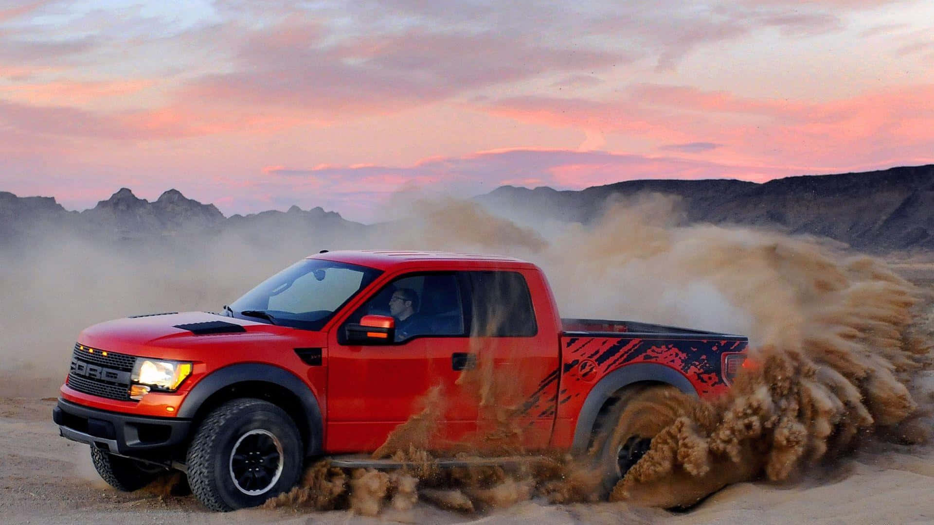 福特 桌布 壁紙 — 一輛紅色福特F-150 Raptor卡車在粉紅色和橙色天空的日落時分穿越沙漠，揚起塵土。