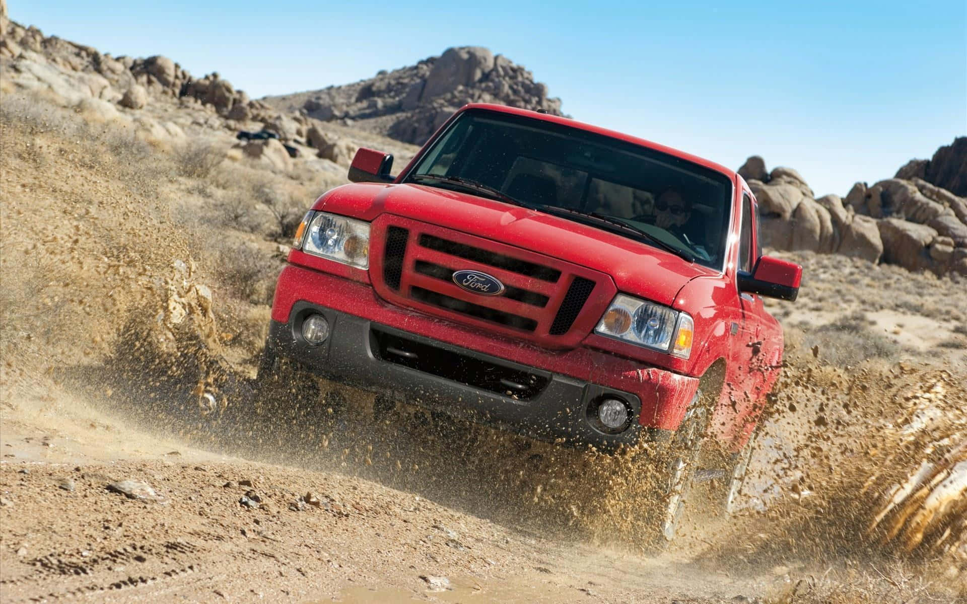 Ford Ranger 桌布 壁紙 — 一輛紅色福特卡車在晴朗藍天下，沿著塵土飛揚的沙漠小徑行駛，揚起沙塵撲向岩石丘陵。