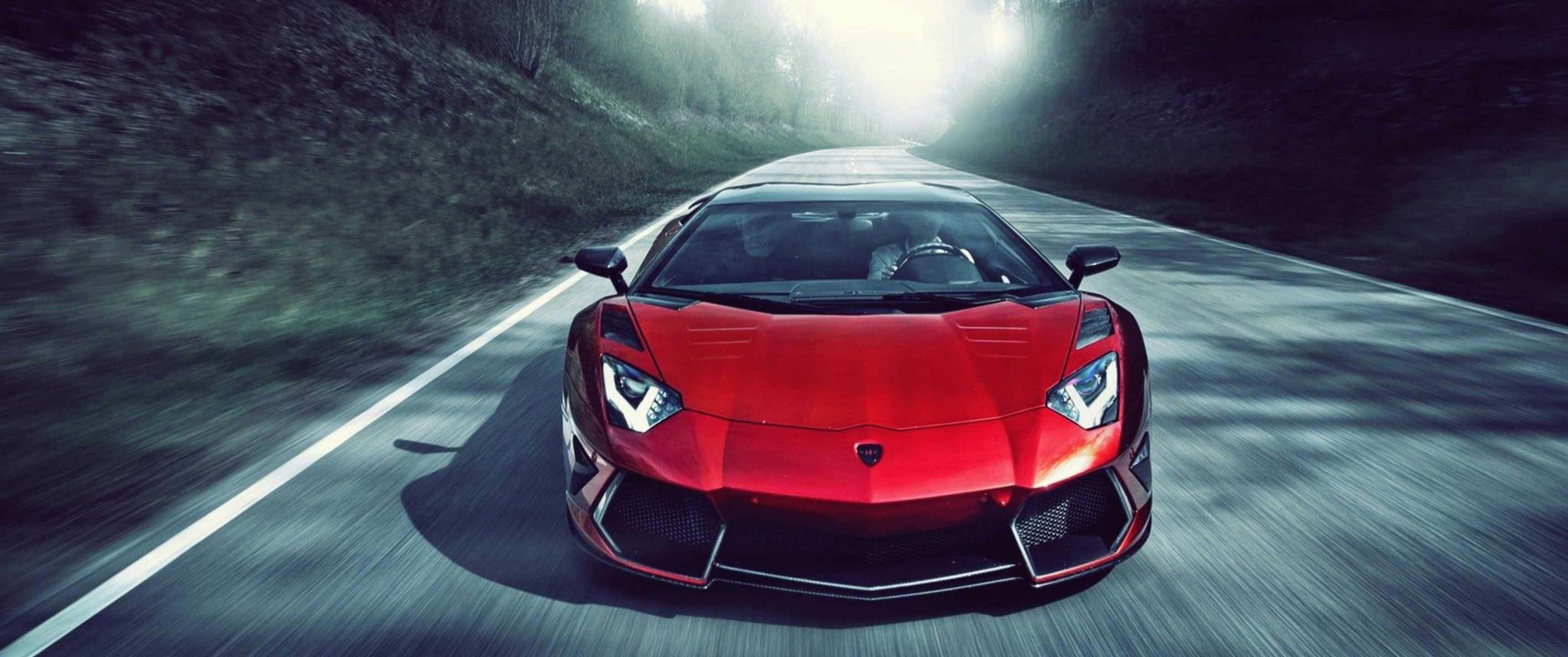 3440x1440p Lamborghini 桌布 壁紙 — 一輛紅色藍寶堅尼Aventador在蜿蜒的林間道路上疾馳，帶有動態模糊和戲劇性的背光效果。